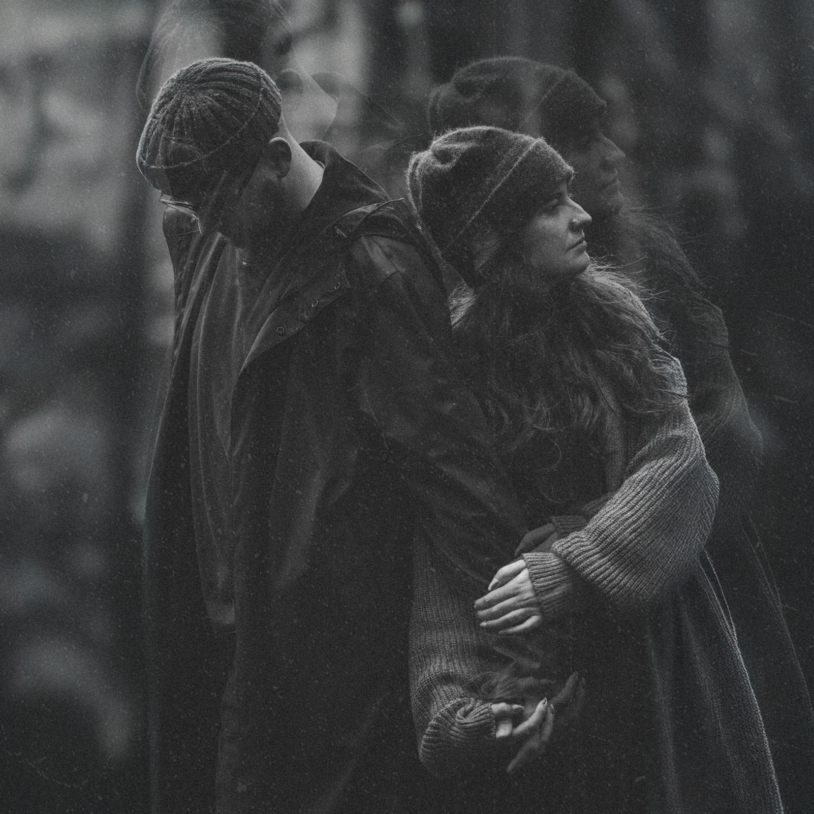 A black and white photo of a woman and a man holding each other, with multiple reflections of their faces in the background, giving a layered effect.