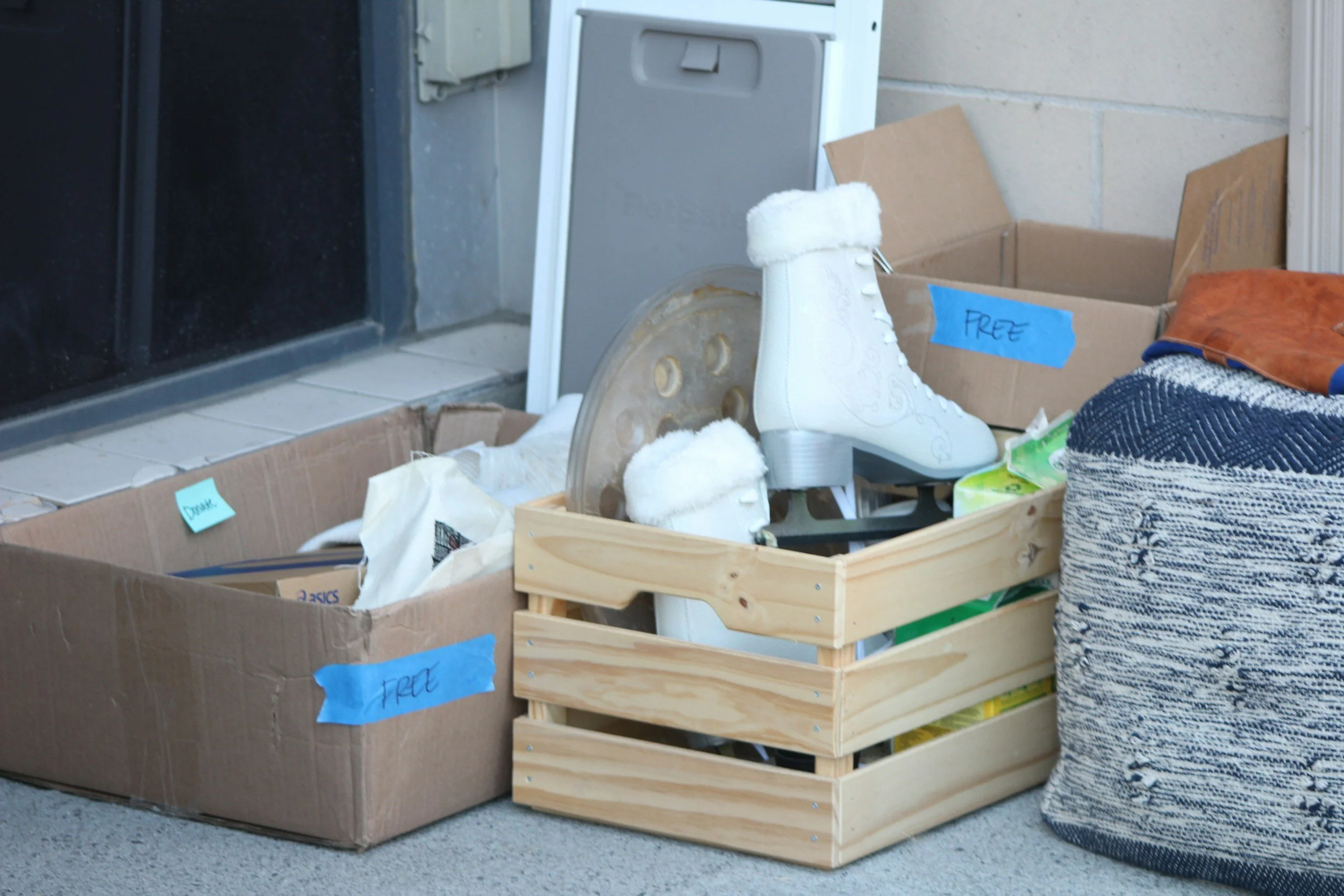 Boxes and a wooden crate labeled "free" holding white ice skates and household items, ready to donate after decluttering