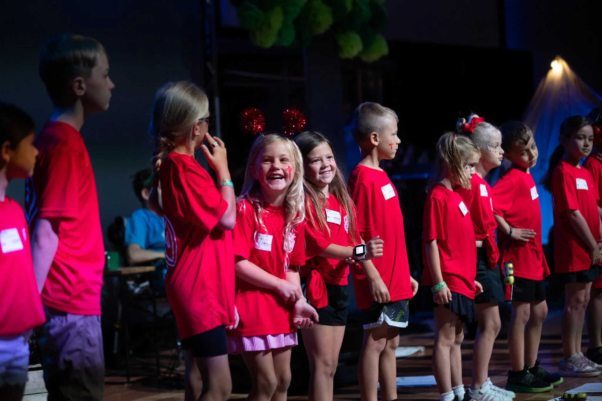 Children dressed in red t-shirts and shorts standing on stage during a performance or event.