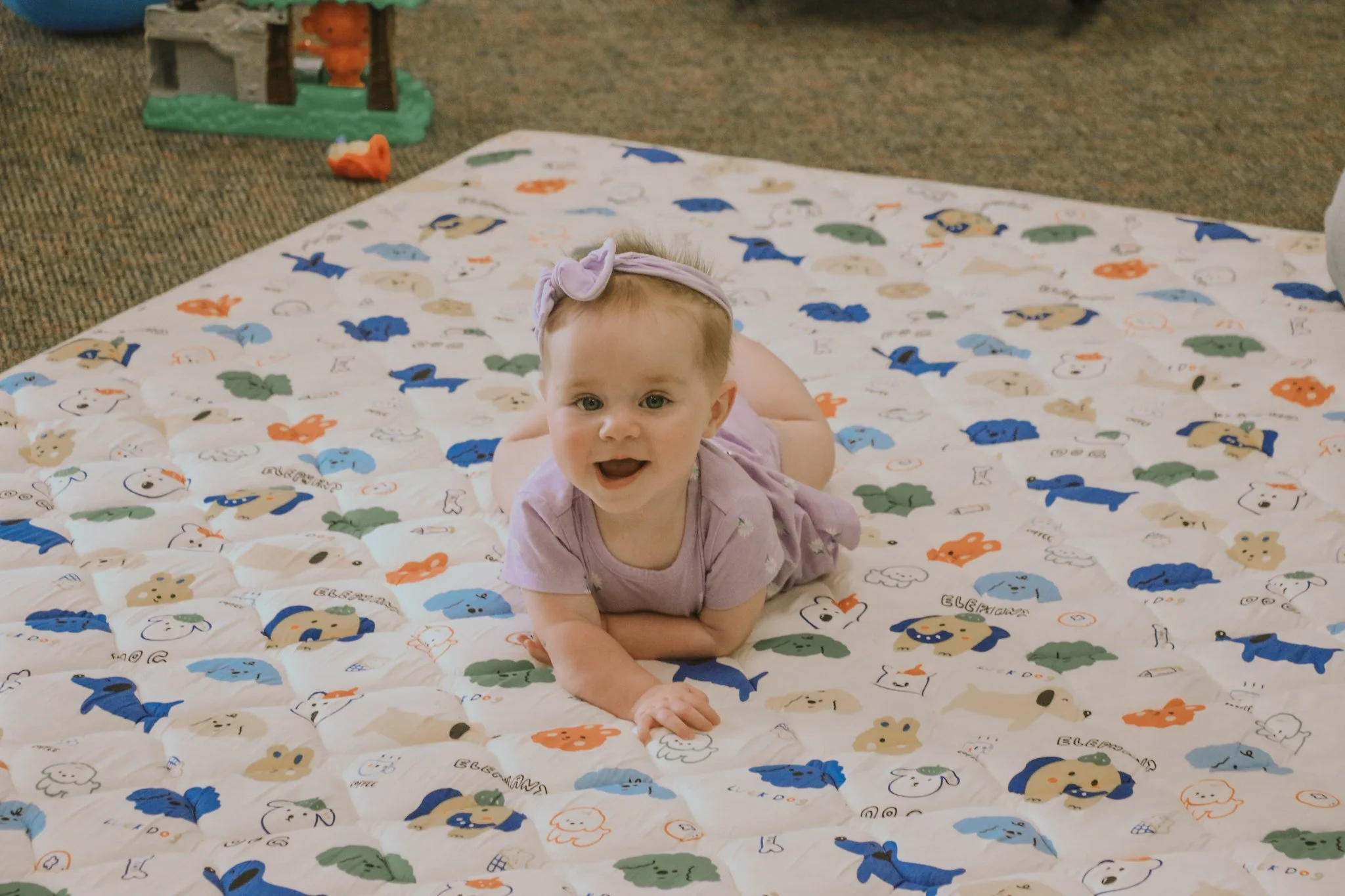 A smiling woman with glasses holding a young child in a room with a rocking chair and a playpen.