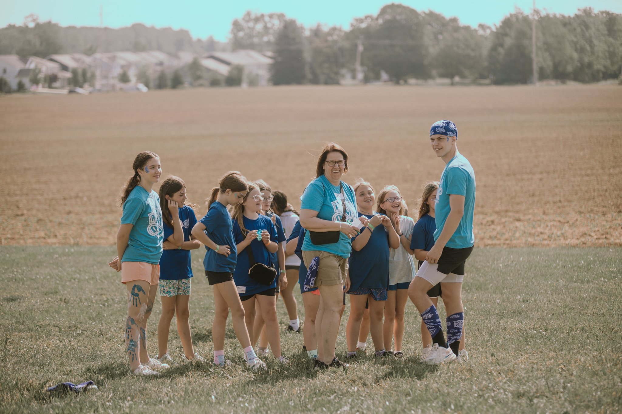 Camp counselor and children standing on a grassy field during daytime.