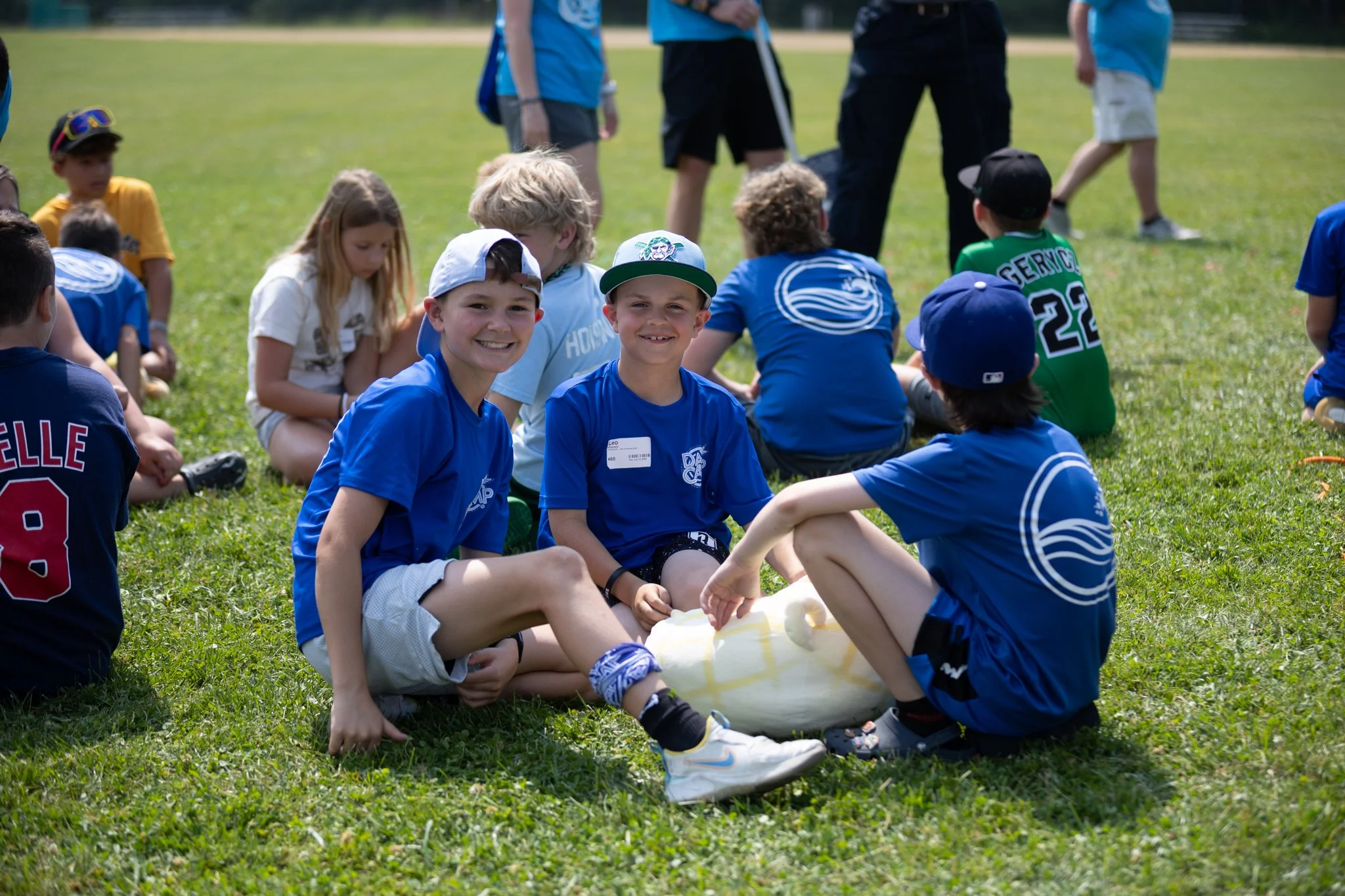 A group of children sitting on the grass at a park, playing with a large white balloon, with some children smiling and others engaged in the activity.