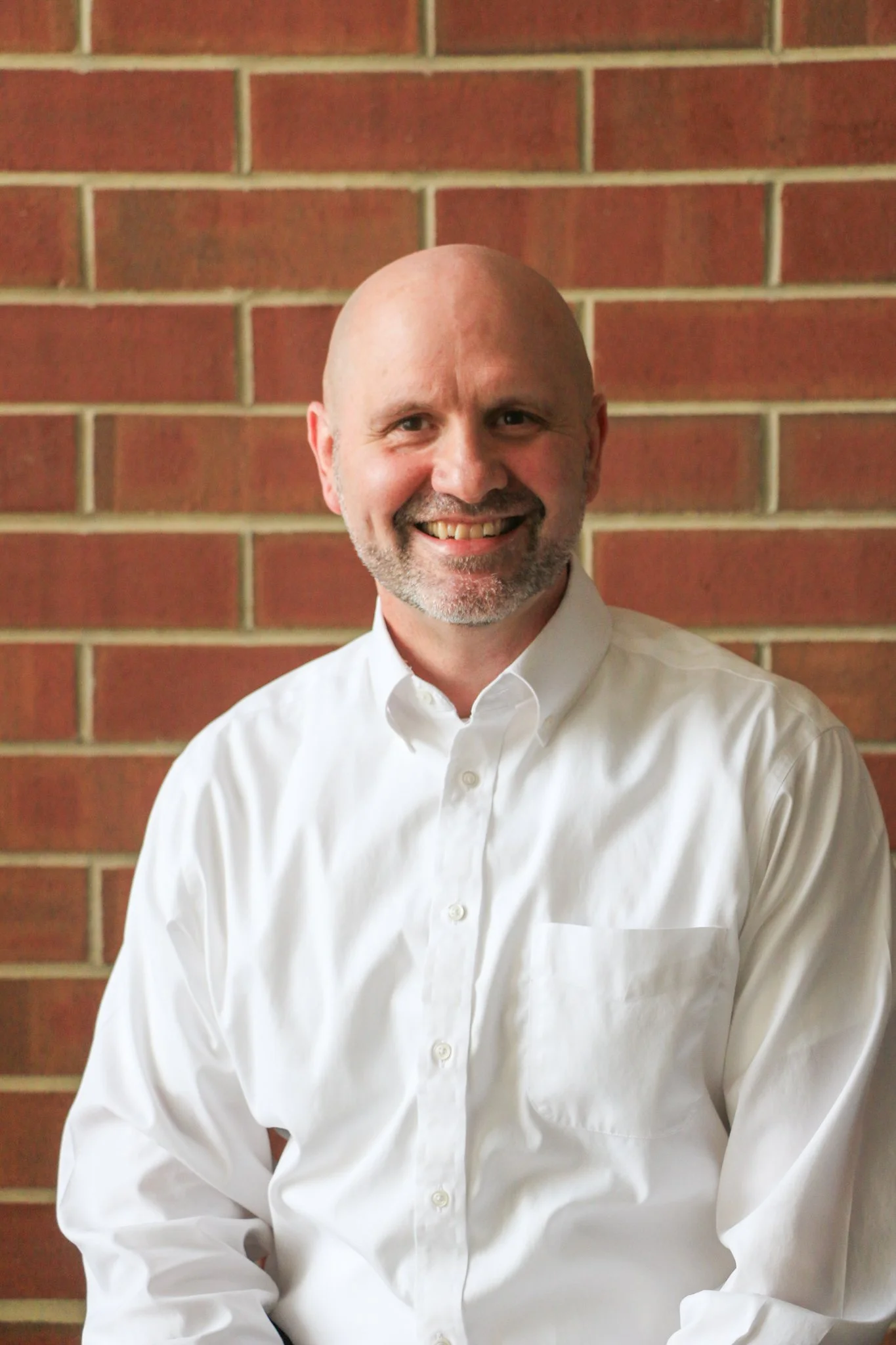 Young man smiling, wearing a black shirt with the text 'Prove Me Wrong!' in front of a wooden wall.