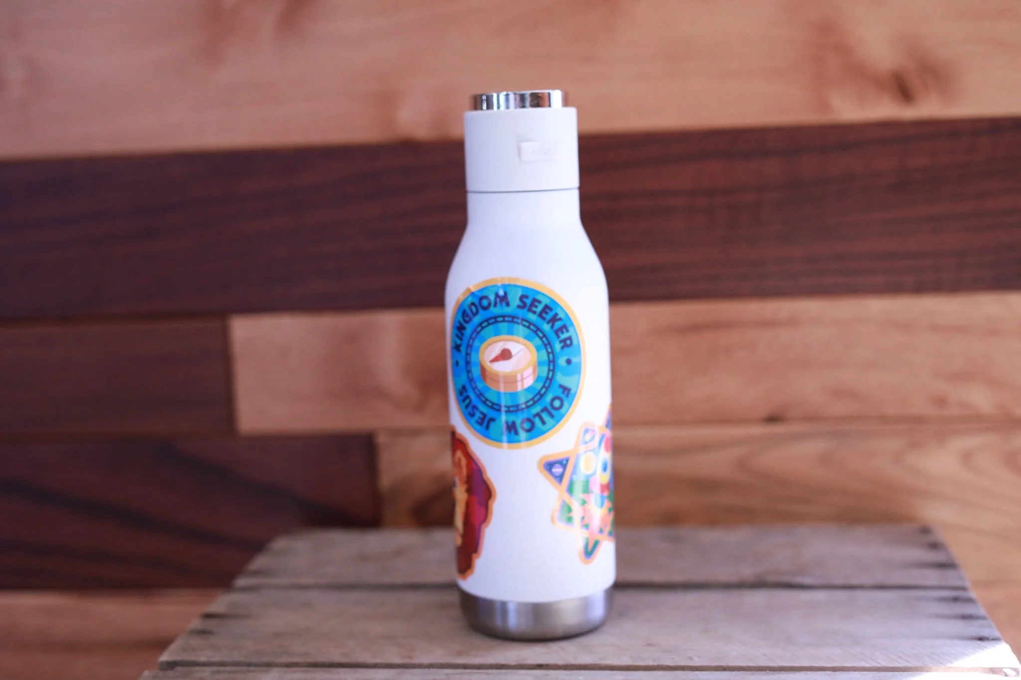 Collection of colorful stickers with camp and motivational themes, including a water bottle with stickers, a 'Love Like Jesus' sticker, a 'Live It Out' sticker, and a small campsite flag.