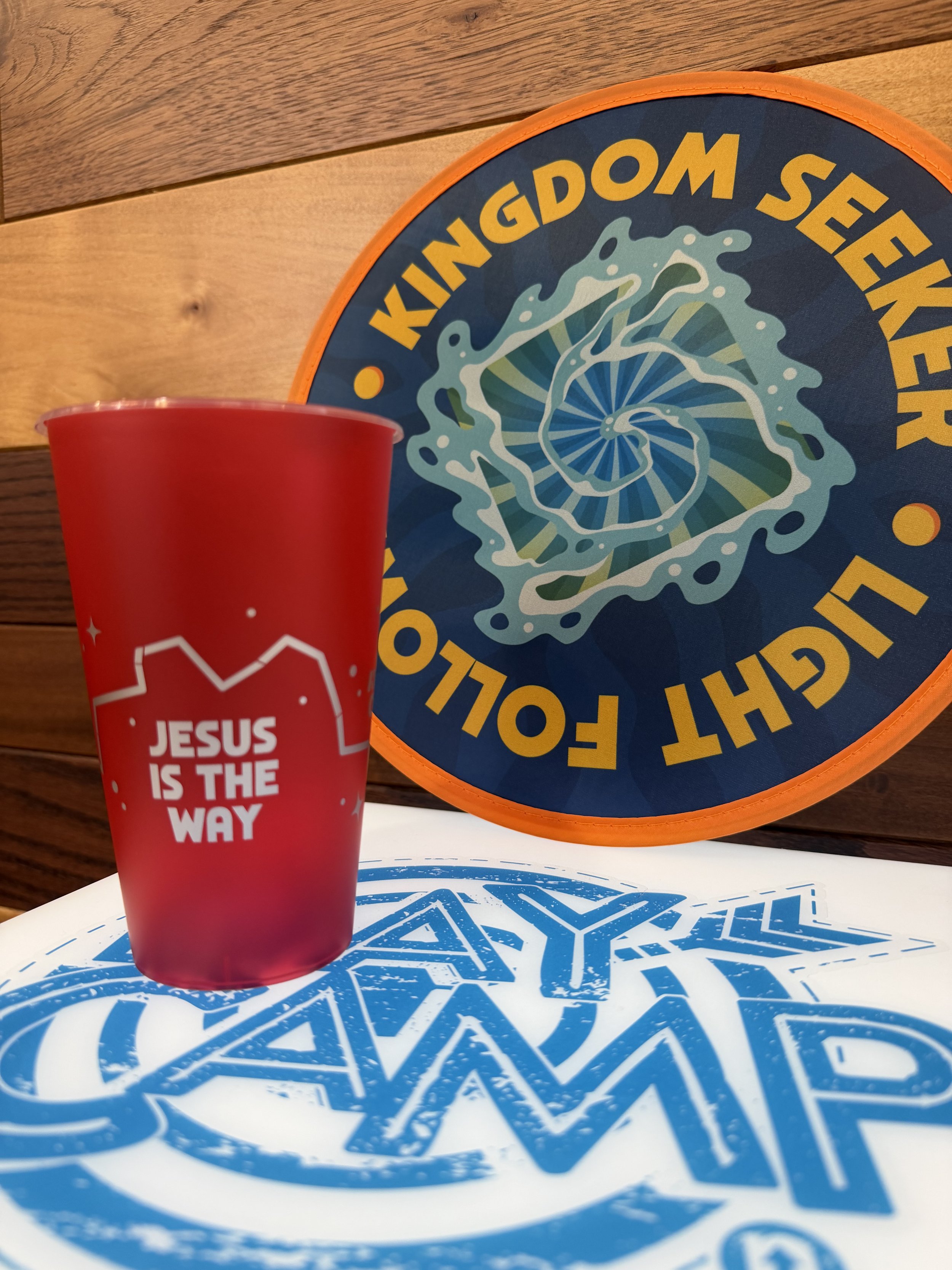 Green cup with the phrase 'LIVE IT OUT' in front of a circular sign that says 'love + life' with cartoon images of a smiling sun and a water bottle.