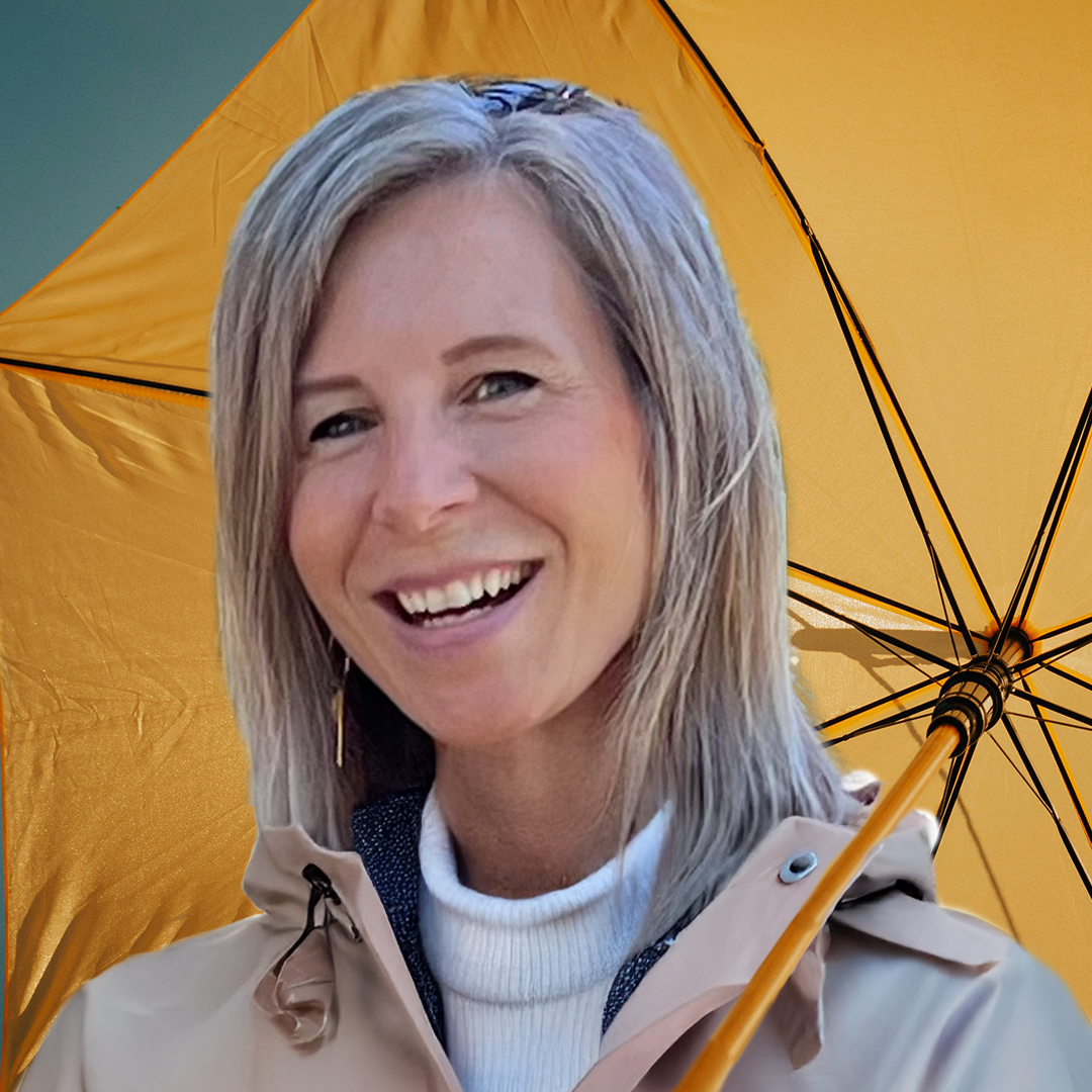 A woman smiling outdoors, holding a yellow umbrella.
