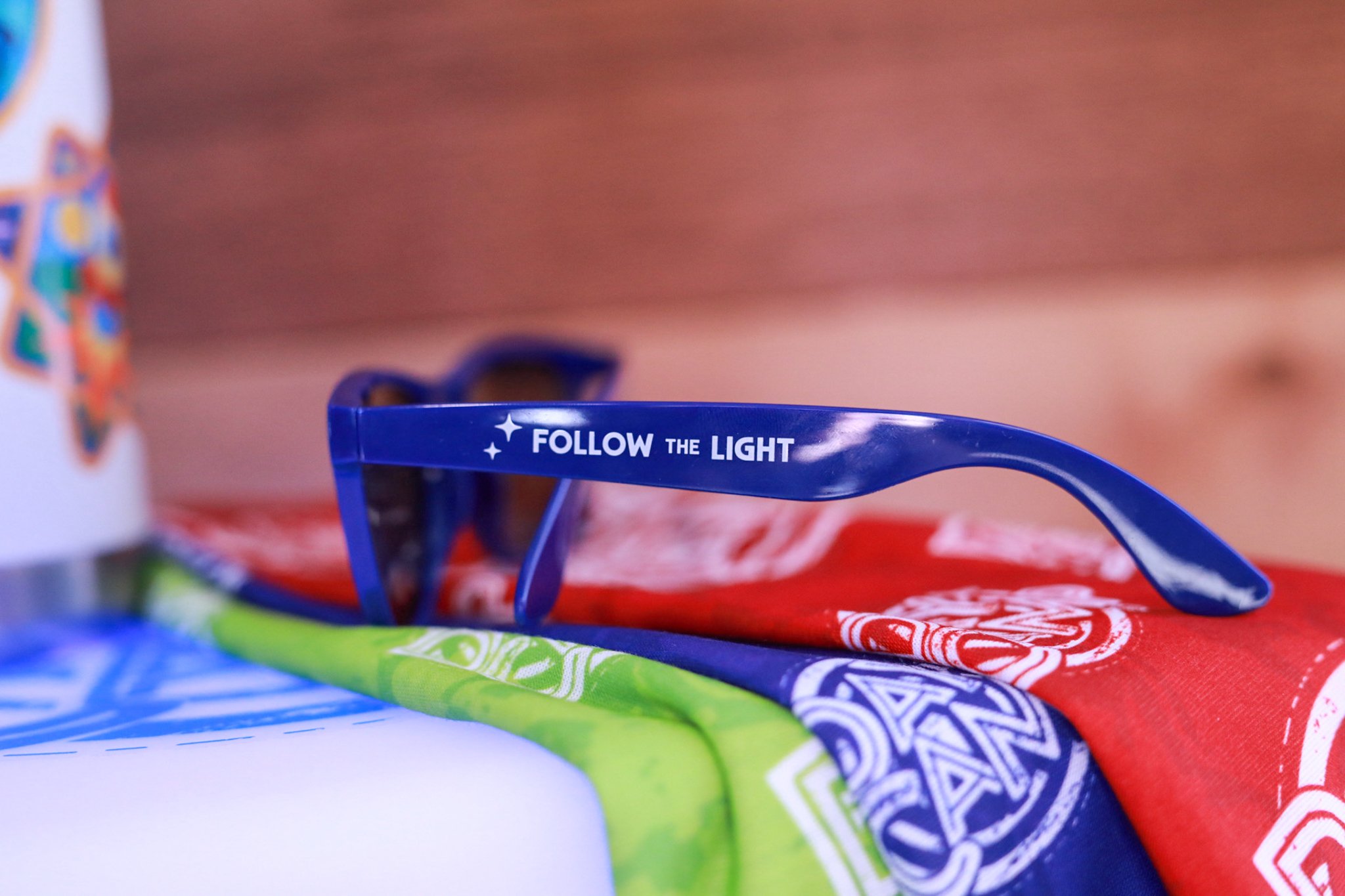 A young girl with long brown hair wearing blue sunglasses, a blue T-shirt, and smiling with braces. She has earrings and a necklace, against a plain white background.