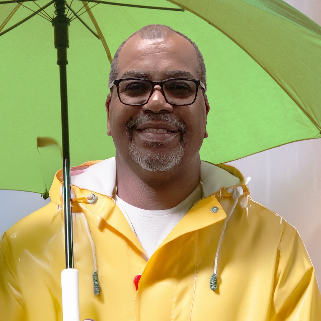 A man wearing glasses and a yellow raincoat holding a green umbrella, smiling.