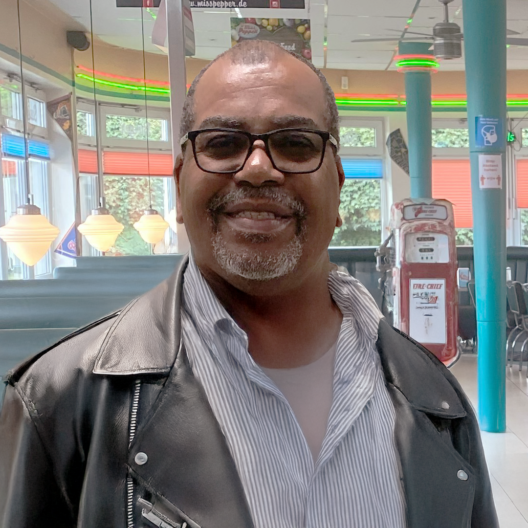 A man wearing glasses and a yellow raincoat holding a green umbrella, smiling.