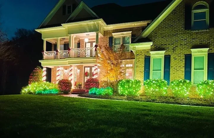house with christmas light in bushes and wrapped around columns