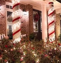 Columns on a house wrapped with white lights and red ribbon