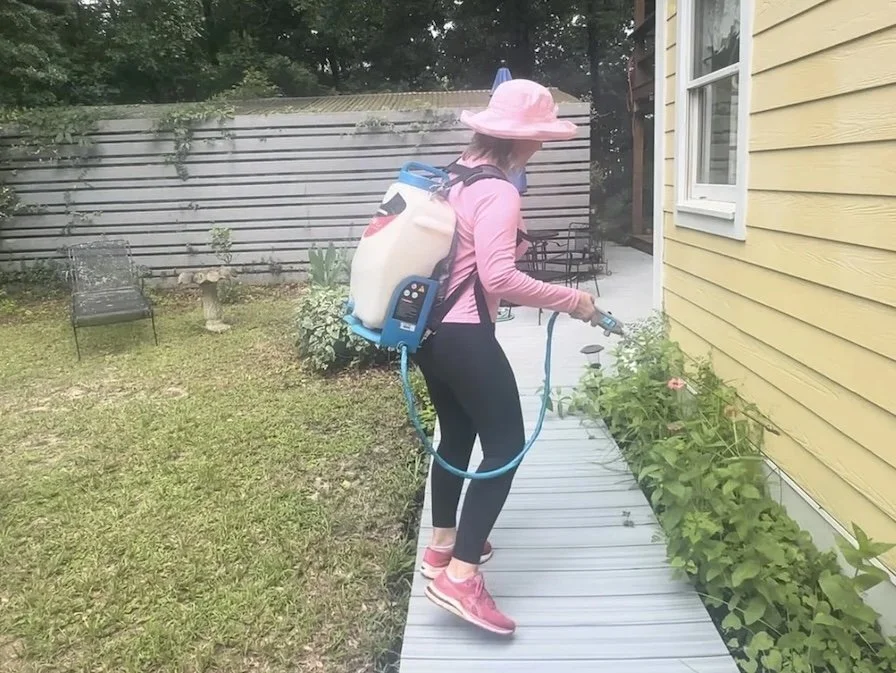 woman spraying insecticide on the exterior of a house