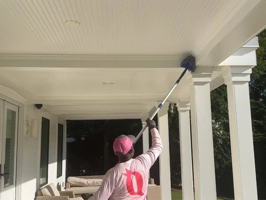 man in pink shirt cleaning cobwebs off house