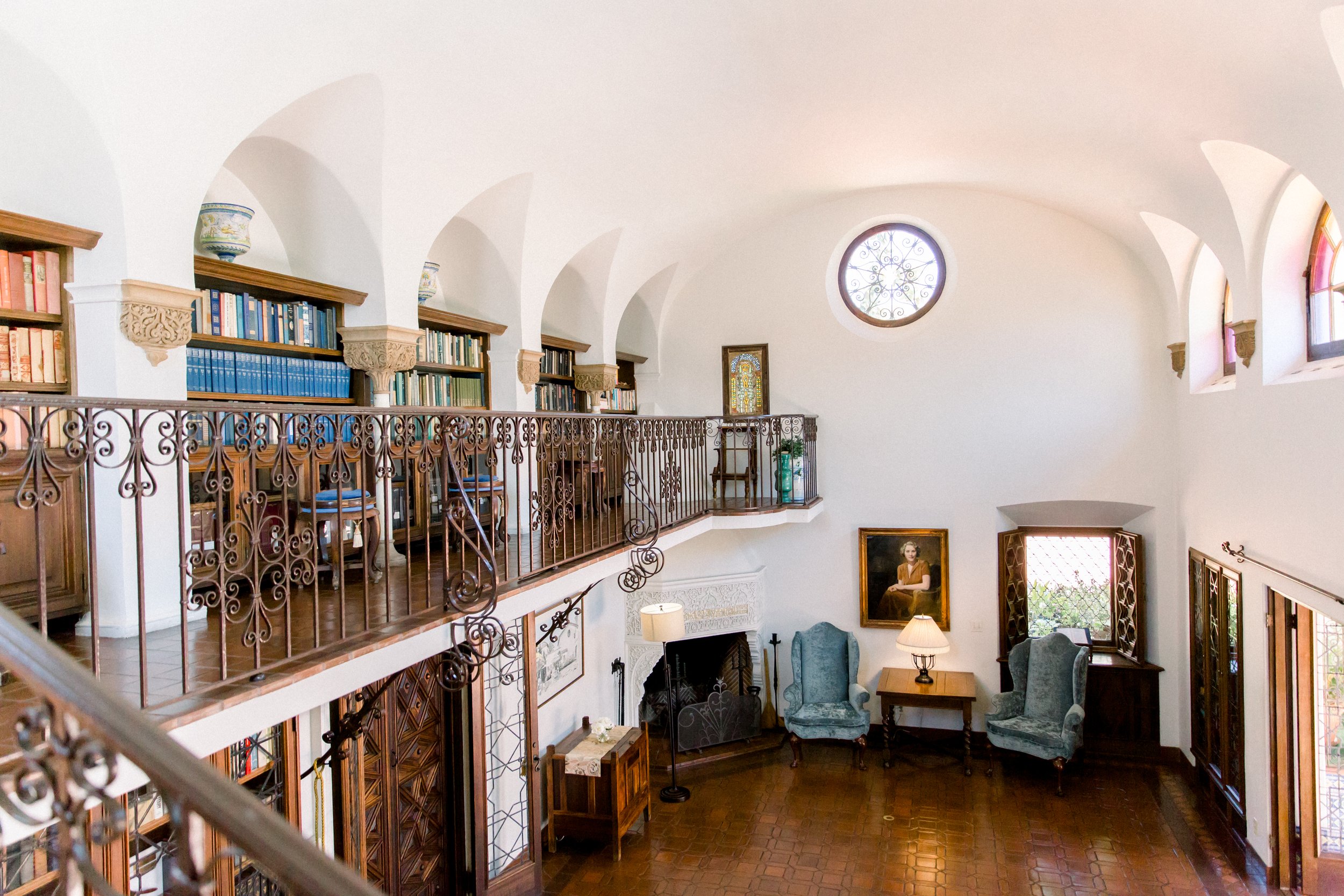 Elegant library with arched ceilings, bookshelves, wrought iron railing, and period furniture.