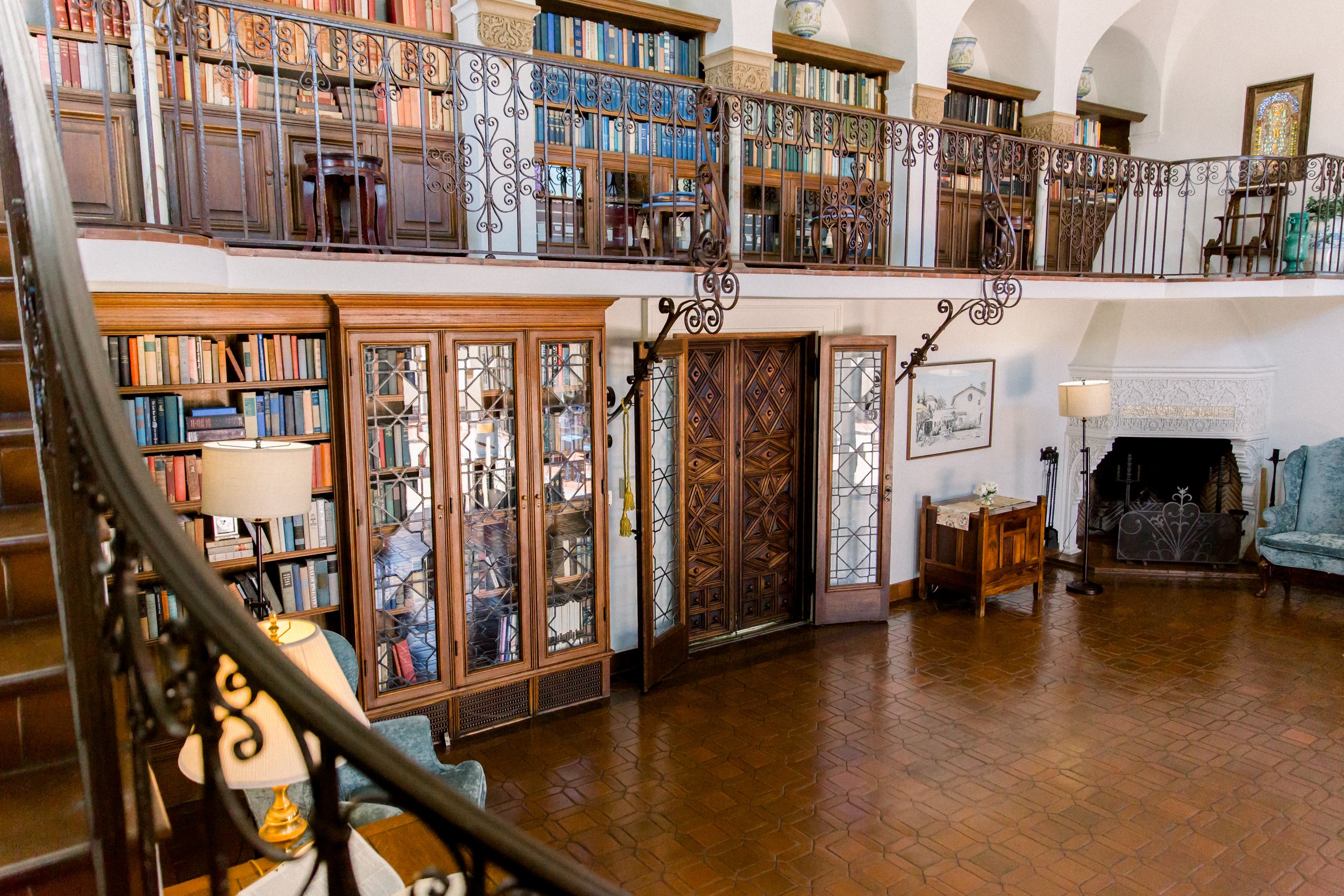 Cozy library room with wooden bookshelves, wrought iron railings, a fireplace, and comfortable seating.