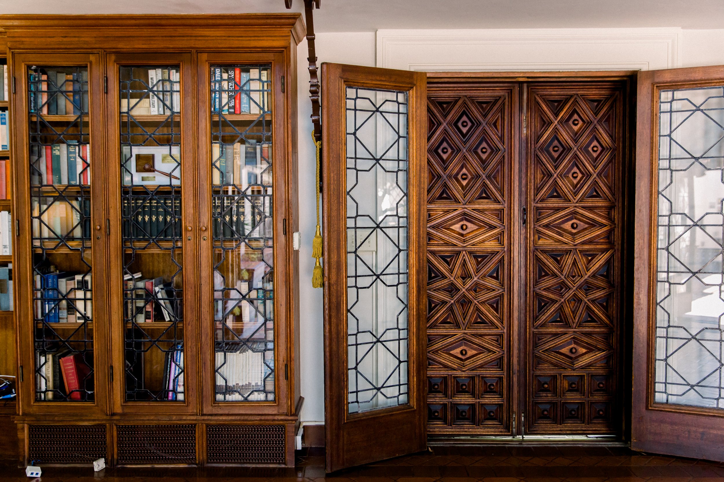 Wooden bookcase with glass doors and intricate geometric design in a room with wooden patterned doors.