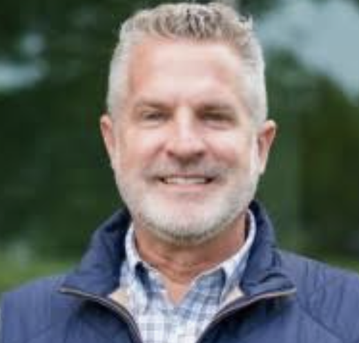 Smiling person wearing a blue jacket and checked shirt, outdoors