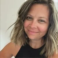A person with shoulder-length wavy hair smiling and wearing a sleeveless black top.
