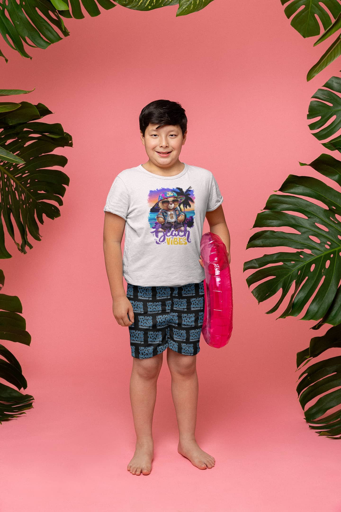 White Beach Vibes t-shirt mockup of a boy wearing sublimated swimming trunks and holding a pool float in a tropical themed background @jellybzz.com
