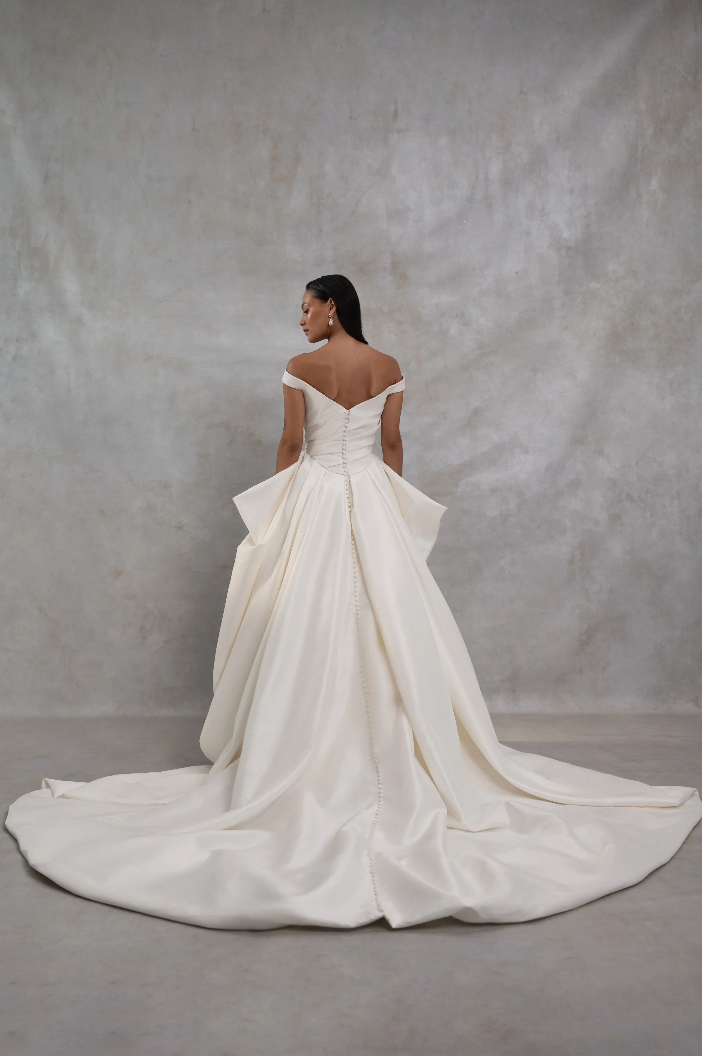 The Jenny Yoo Bridal Elle gown, cut in our lofty Italian taffeta, is a true chameleon. Featuring a corseted bodice with a flattering Basque waist and a delicate off the shoulder strap, her voluminous skirt transforms into a dramatic high-low look per