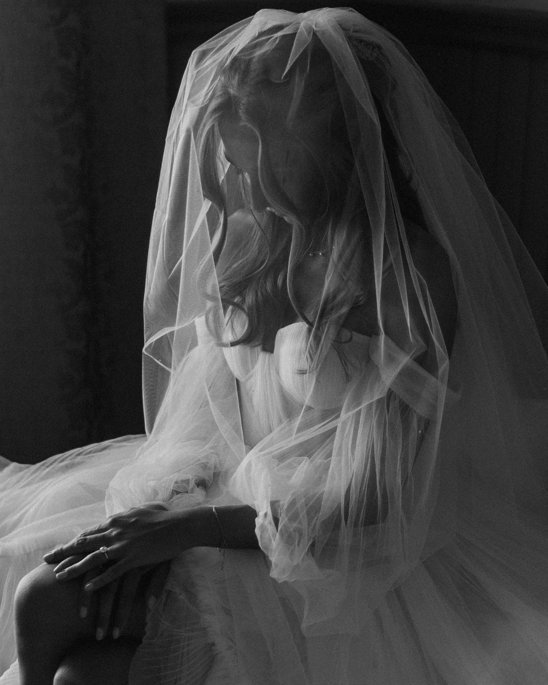 A woman wearing a veil and a wedding dress, sitting with her eyes closed.