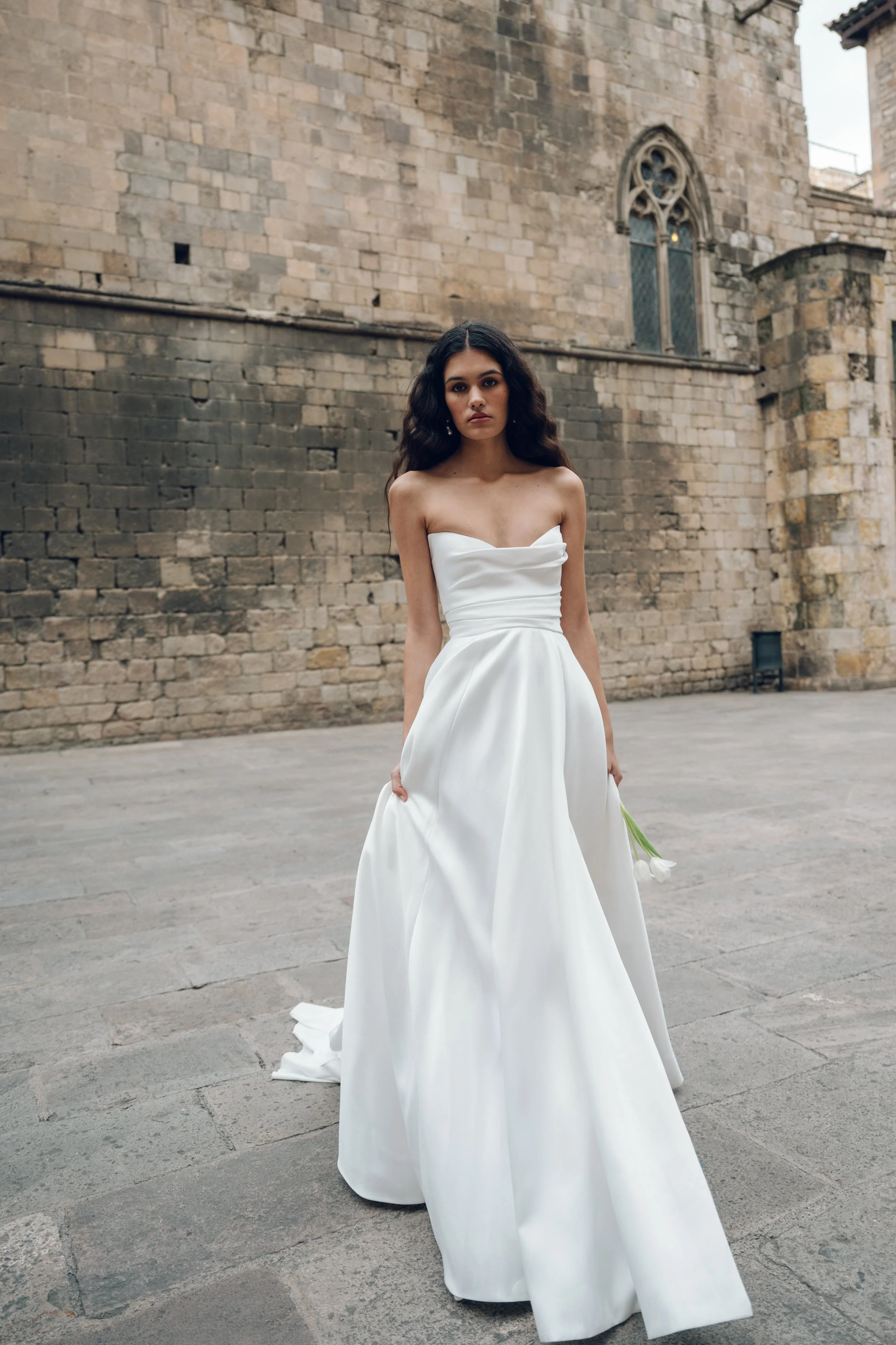 The Jenny Yoo Marisol gown is a romantic satin ball gown with a beautifully draped bodice and a sultry, sculpted cowl neckline that feels effortlessly feminine. It features a full skirt interrupted by a flattering slit and comes with detachable puff 