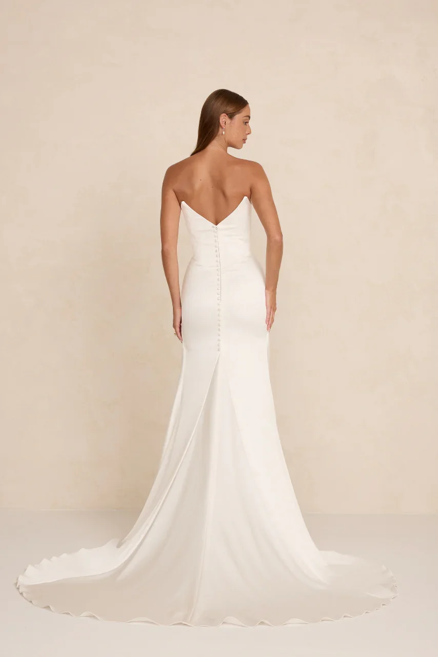 The MWL Natalie is crafted from two layers of Crepe Satin with a fluid drape and soft sheen. A cinched scooped bodice defines the waist, while a pinched front and illustrious fabric creates an exceptional bridal look. Natalie will be available at Hal