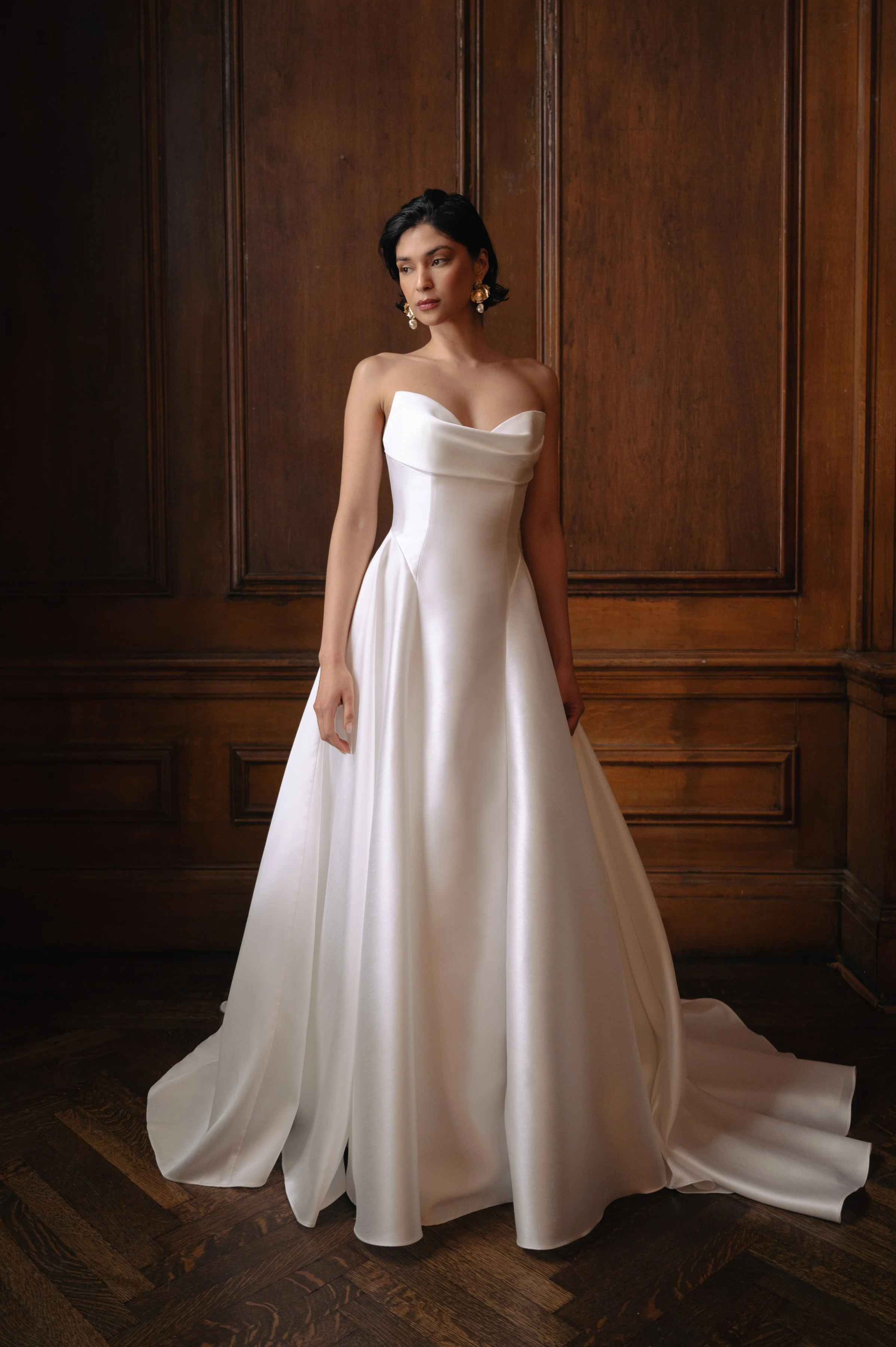 The Jenny Yoo Romina gown is a refined strapless A-line wedding dress crafted from lightweight, luminous canopy taffeta with a beautifully draped cowl bodice and sculpted drop-waist silhouette that feels both modern and timeless. Its soft, elegant li