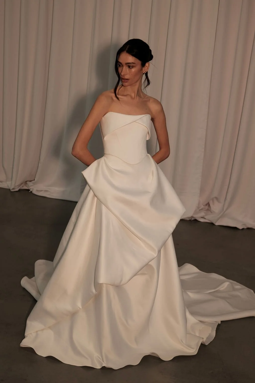 KYHA Bride Preston: an ode to eras past. A fresh take on tradition, Preston brings a modern edge thanks to its structural draping, showstopping train and architectural dropped waist. Crafted from luxe silk satin, Preston’s strapless silhouette, struc