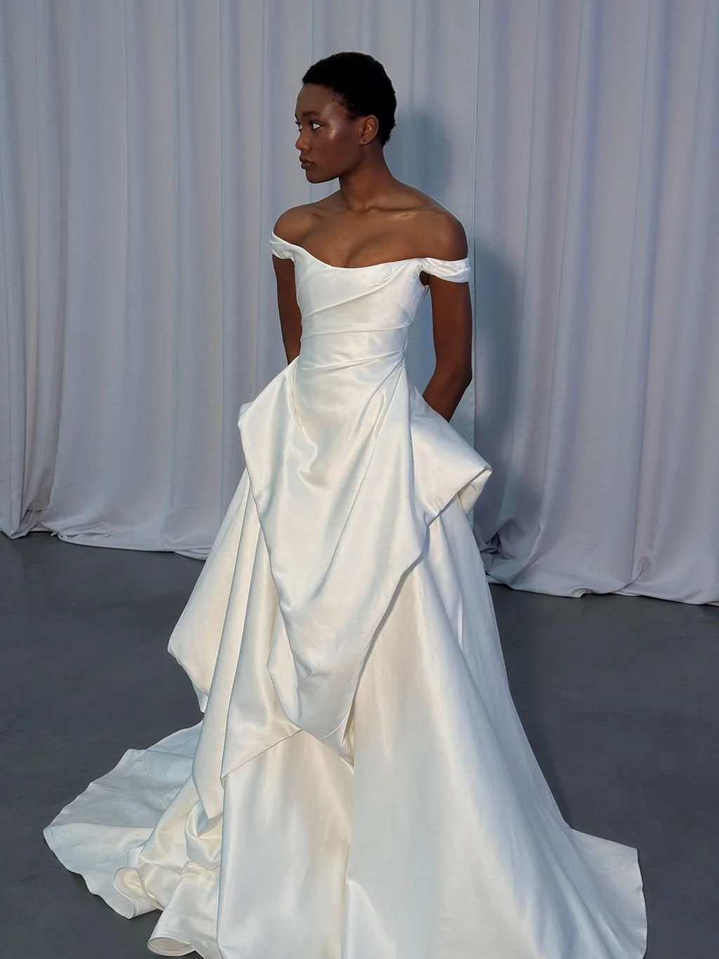 Cool girls wear KYHA Bride Willis. Luxe ivory silk satin is directionally draped across the front bodice and crafted into architectural side folds in a celebration of the female form. A full draped skirt and a sweeping train create a more-is-more sta