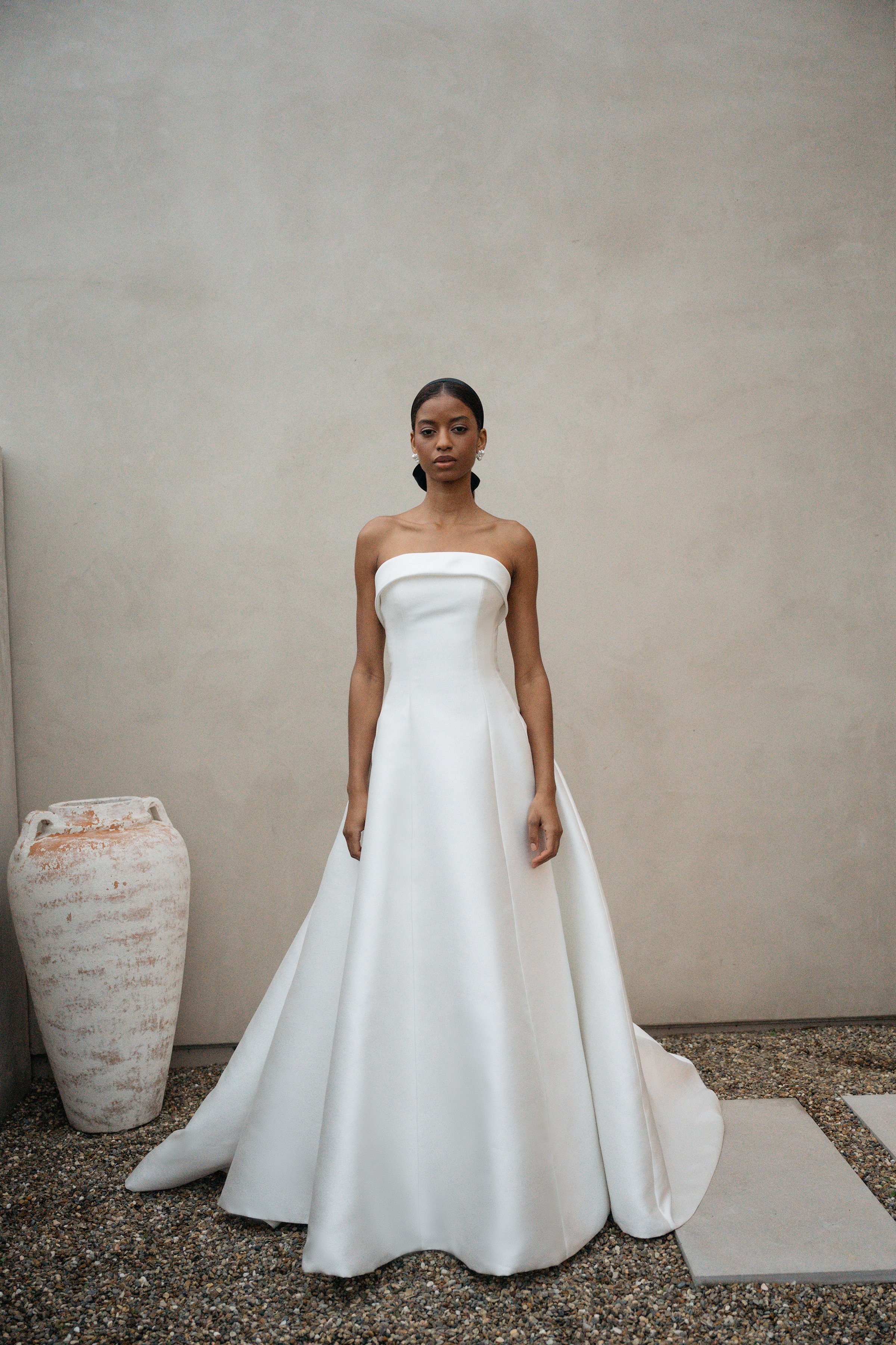 The Jenny Yoo Bridal Leah gown is a chic, timeless design in sleek Mikado that proves less is more, featuring a straight strapless neckline with subtle band detail and flattering princess seams. Its clean A-line silhouette with covered buttons down t