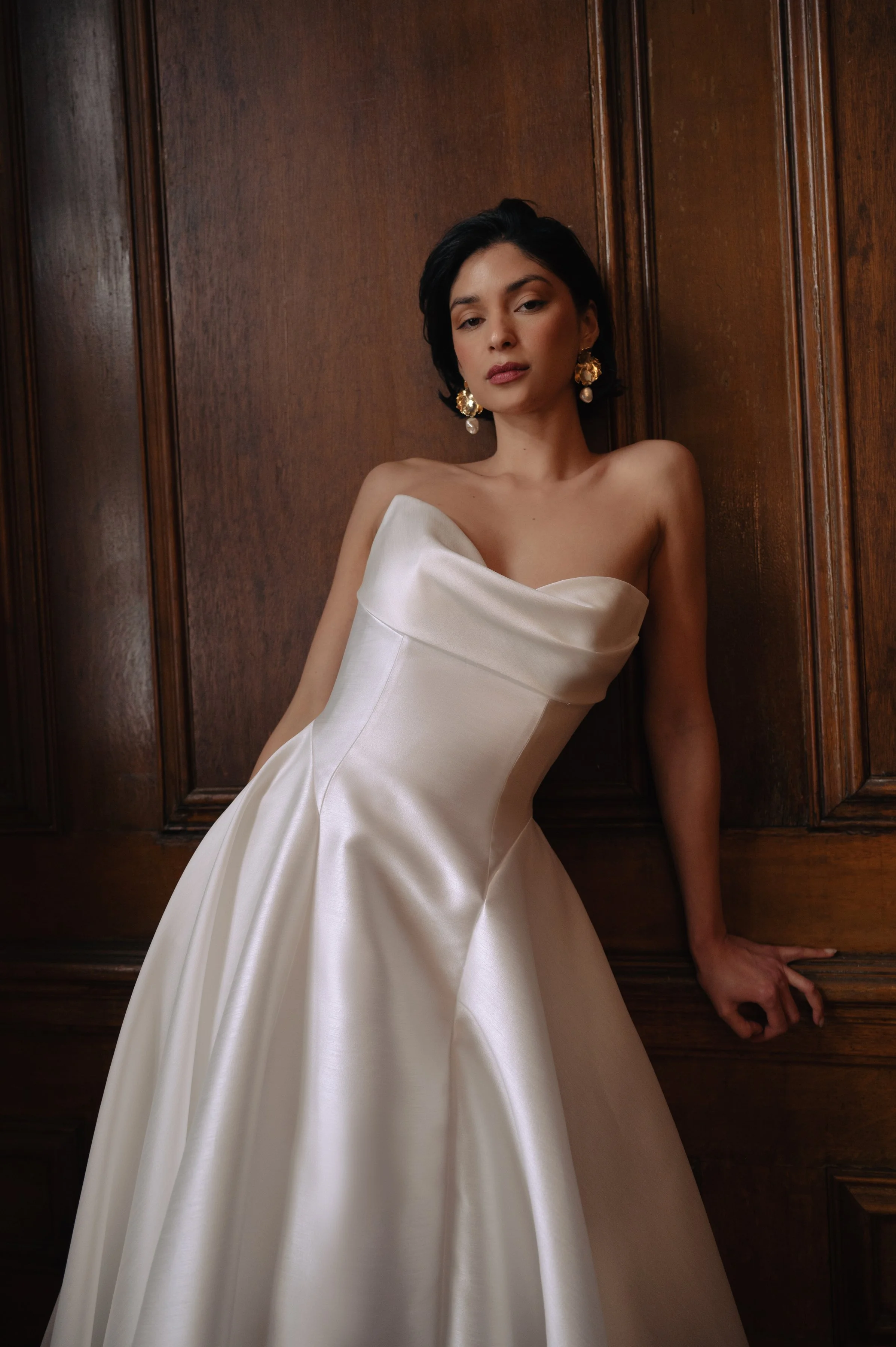 The Jenny Yoo Romina gown is a refined strapless A-line wedding dress crafted from lightweight, luminous canopy taffeta with a beautifully draped cowl bodice and sculpted drop-waist silhouette that feels both modern and timeless. Its soft, elegant li