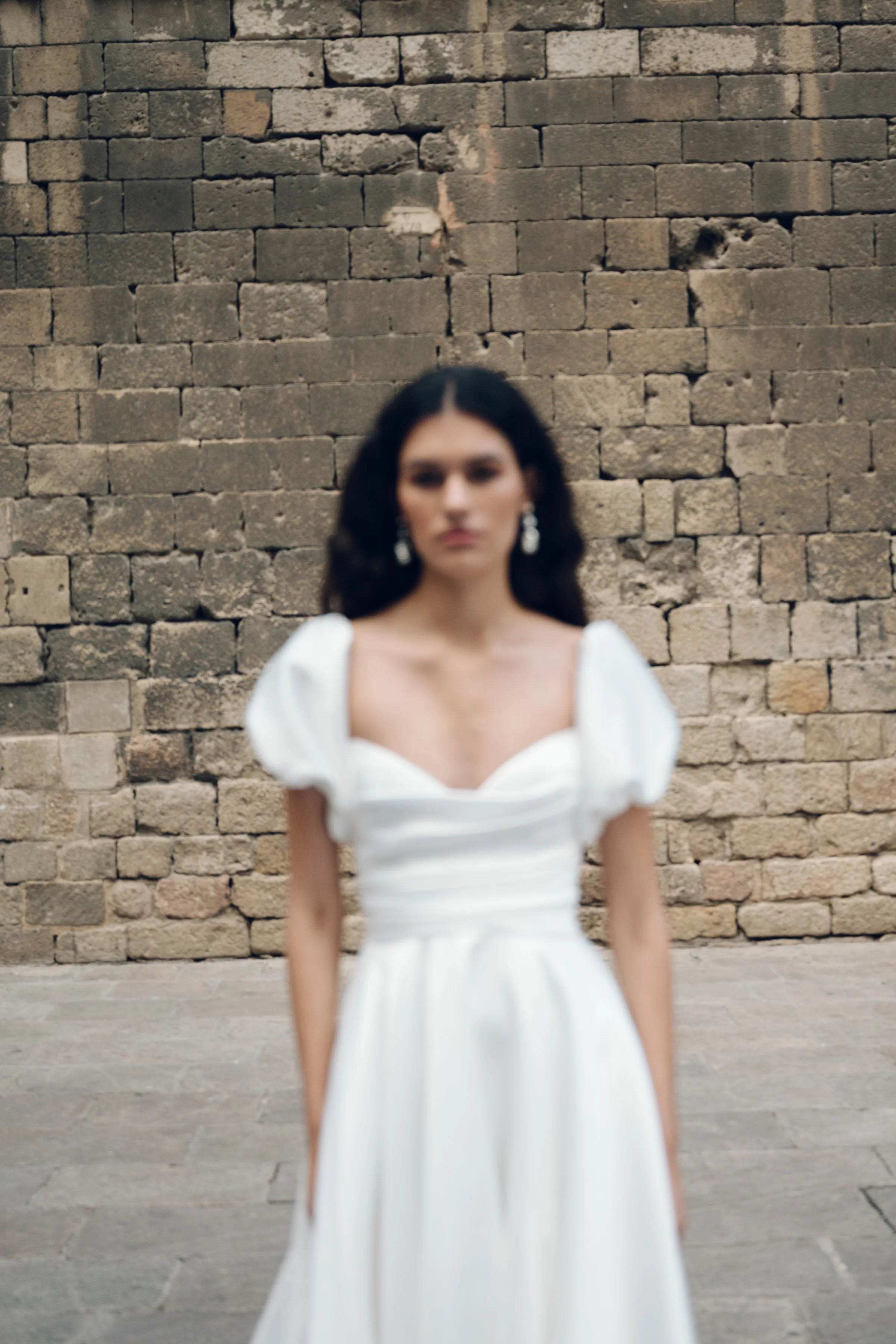 The Jenny Yoo Marisol gown is a romantic satin ball gown with a beautifully draped bodice and a sultry, sculpted cowl neckline that feels effortlessly feminine. It features a full skirt interrupted by a flattering slit and comes with detachable puff 