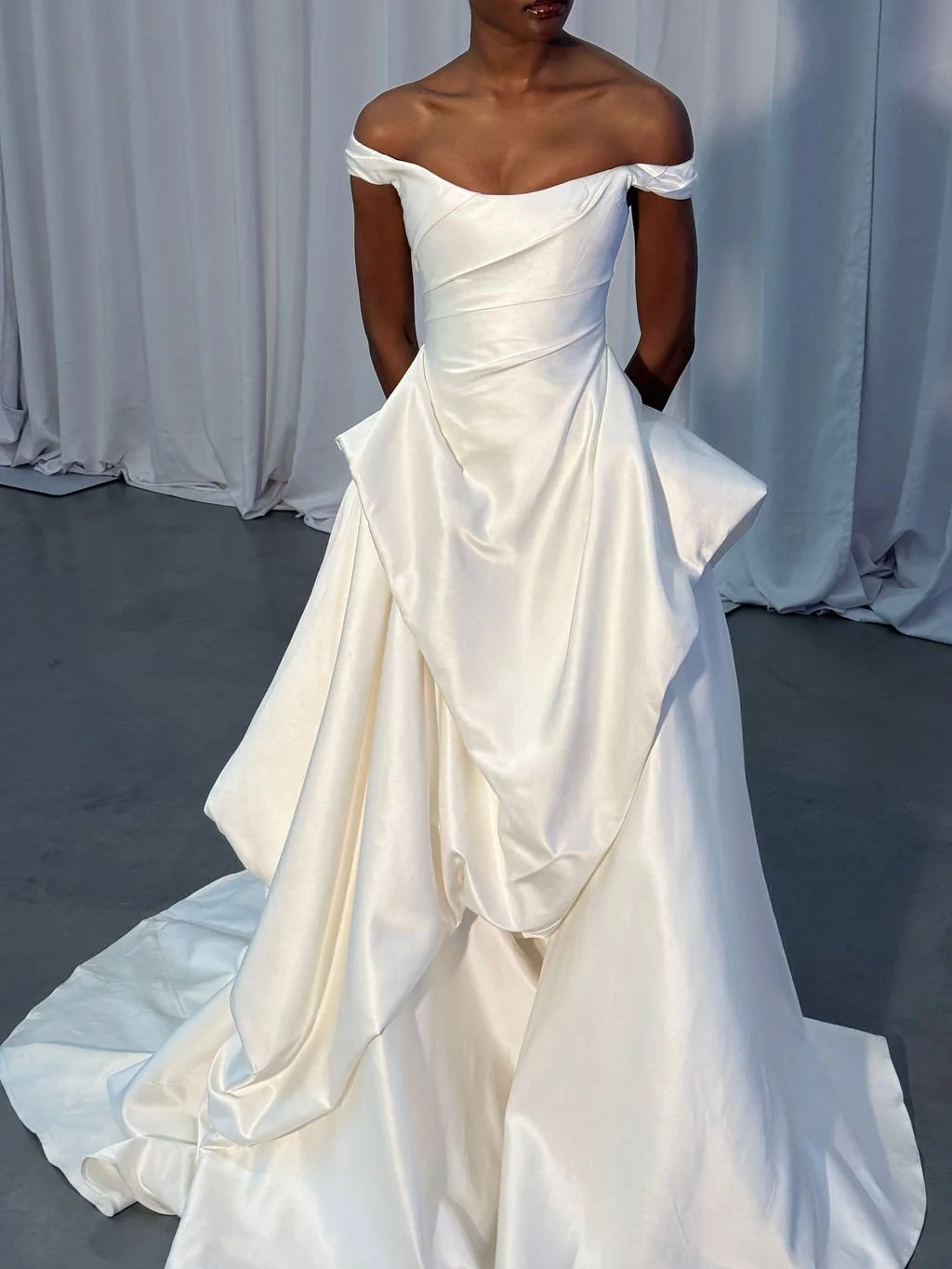 Cool girls wear KYHA Bride Willis. Luxe ivory silk satin is directionally draped across the front bodice and crafted into architectural side folds in a celebration of the female form. A full draped skirt and a sweeping train create a more-is-more sta