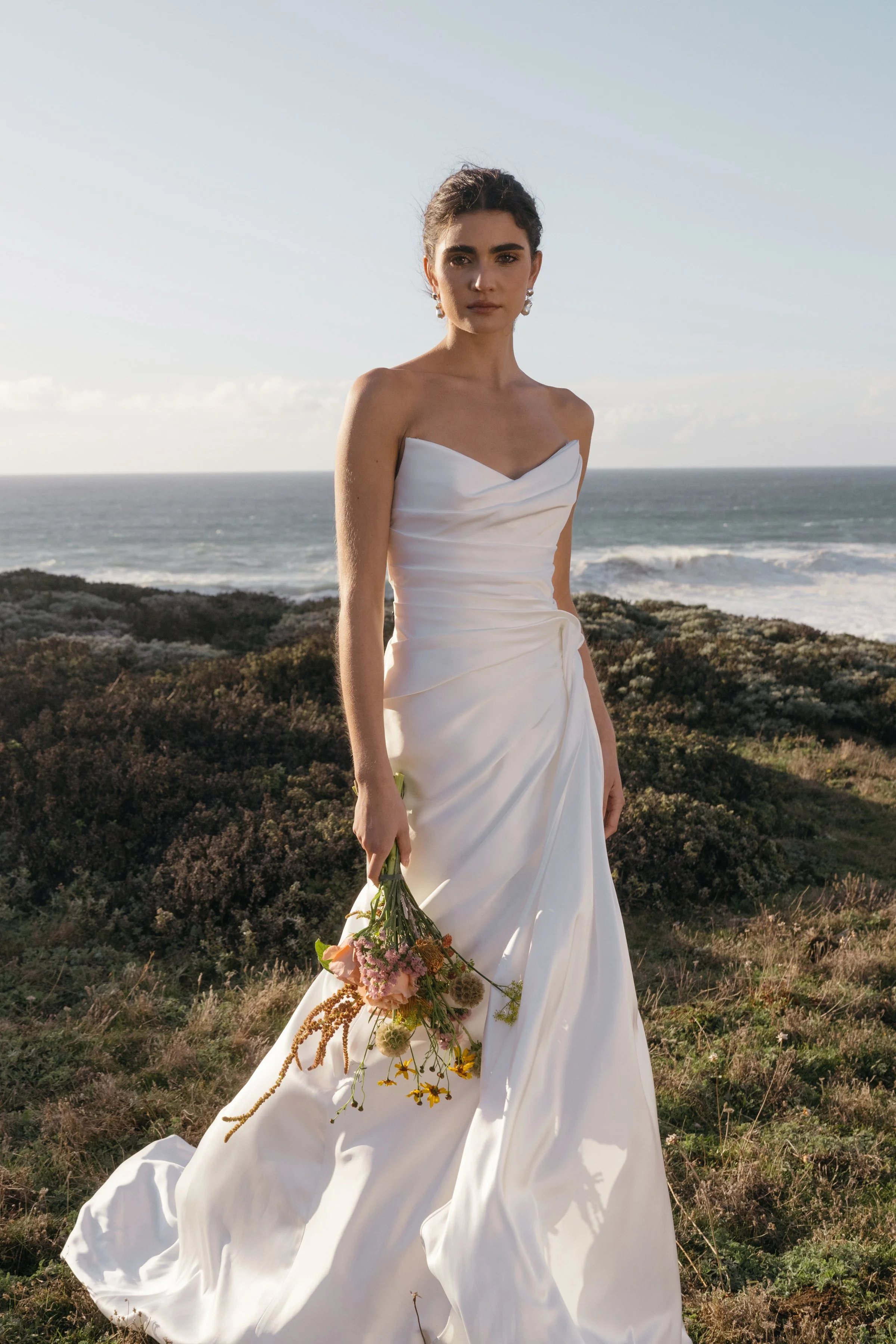 The Jenny Yoo Lana gown is a refined satin wedding dress cut in luminous Barcelona satin with elegant pleating and draping that flatters the figure, and it stands out for its versatile styling with removable long sleeves and optional sash sleeves tha