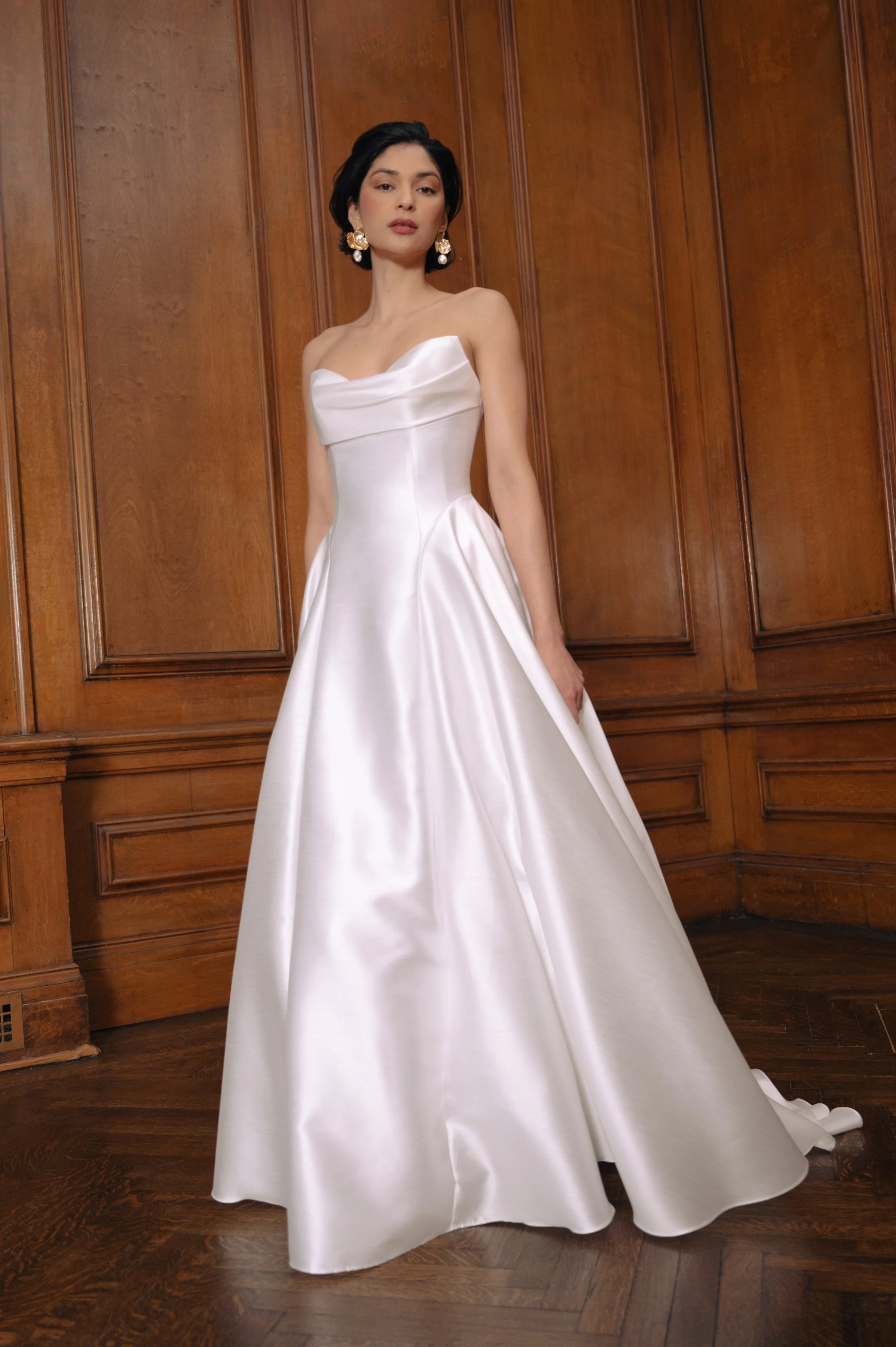 The Jenny Yoo Romina gown is a refined strapless A-line wedding dress crafted from lightweight, luminous canopy taffeta with a beautifully draped cowl bodice and sculpted drop-waist silhouette that feels both modern and timeless. Its soft, elegant li