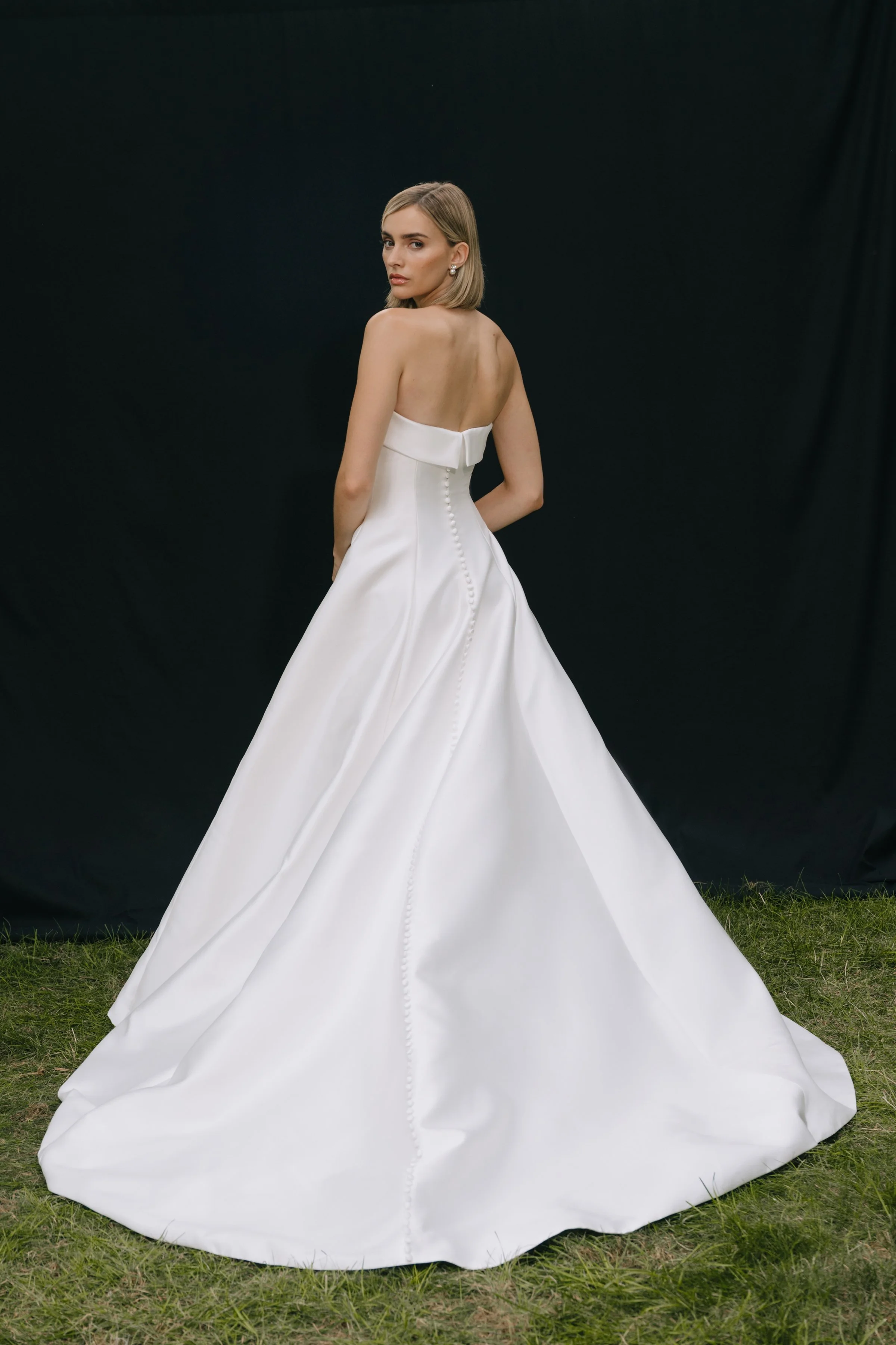 The Jenny Yoo Bridal Leah gown is a chic, timeless design in sleek Mikado that proves less is more, featuring a straight strapless neckline with subtle band detail and flattering princess seams. Its clean A-line silhouette with covered buttons down t