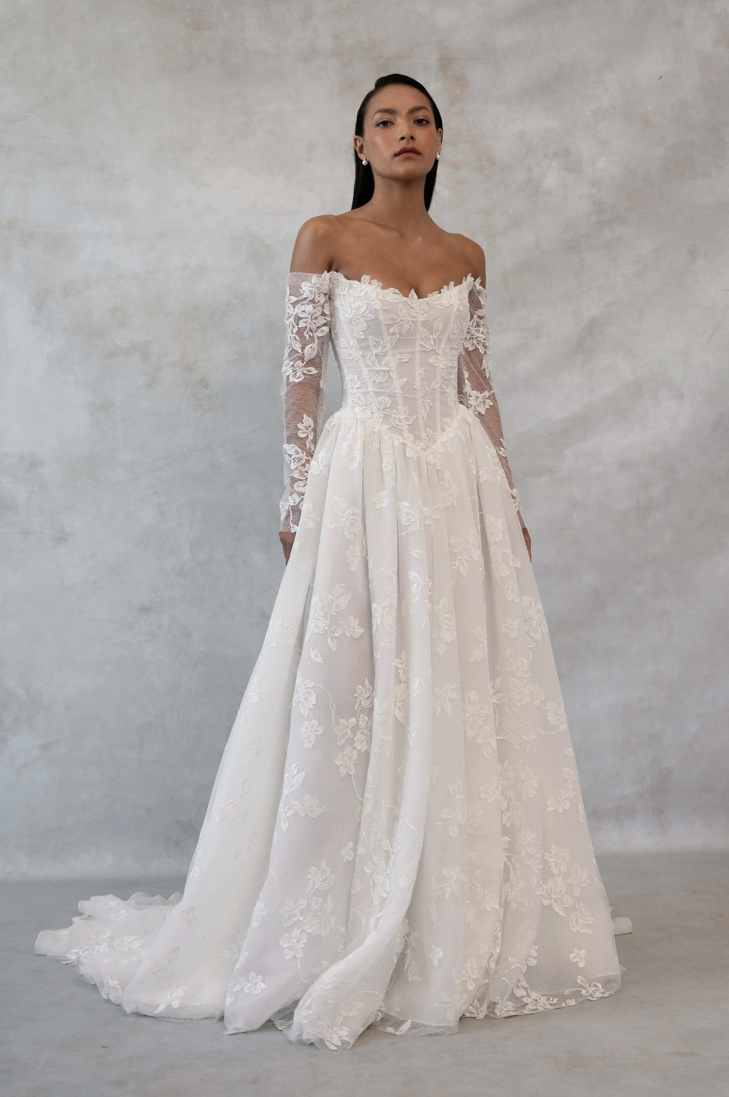 The Jenny Yoo Phoebe gown, cut in our delicately textured Isadora floral embroidery, is as modern as she is romantic. The structured Basque corset bodice leads way to a flowing gathered skirt. Detachable long sleeves lend exciting versatility.