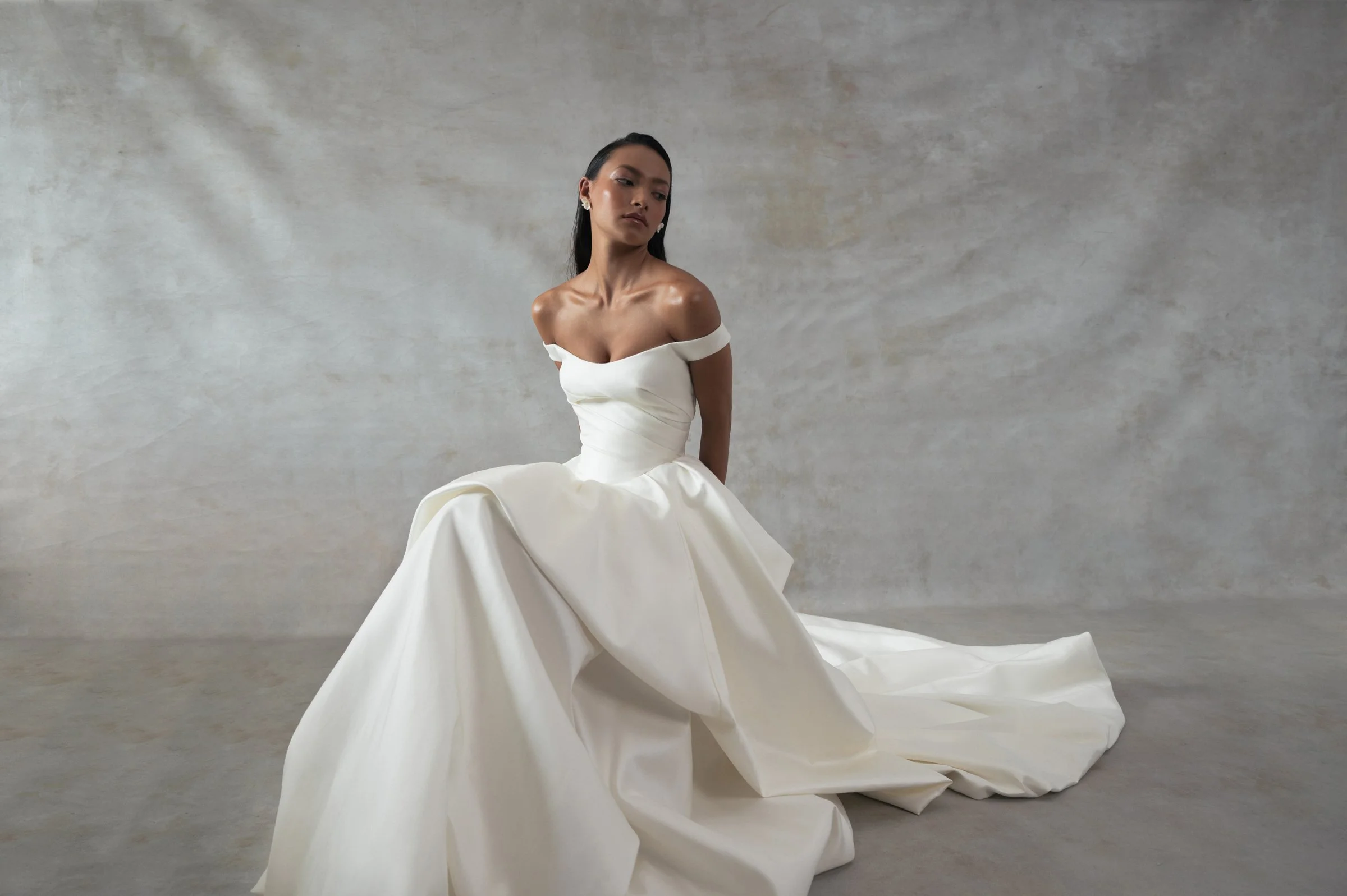 The Jenny Yoo Bridal Elle gown, cut in our lofty Italian taffeta, is a true chameleon. Featuring a corseted bodice with a flattering Basque waist and a delicate off the shoulder strap, her voluminous skirt transforms into a dramatic high-low look per