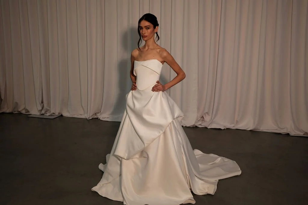 KYHA Bride Preston: an ode to eras past. A fresh take on tradition, Preston brings a modern edge thanks to its structural draping, showstopping train and architectural dropped waist. Crafted from luxe silk satin, Preston’s strapless silhouette, struc