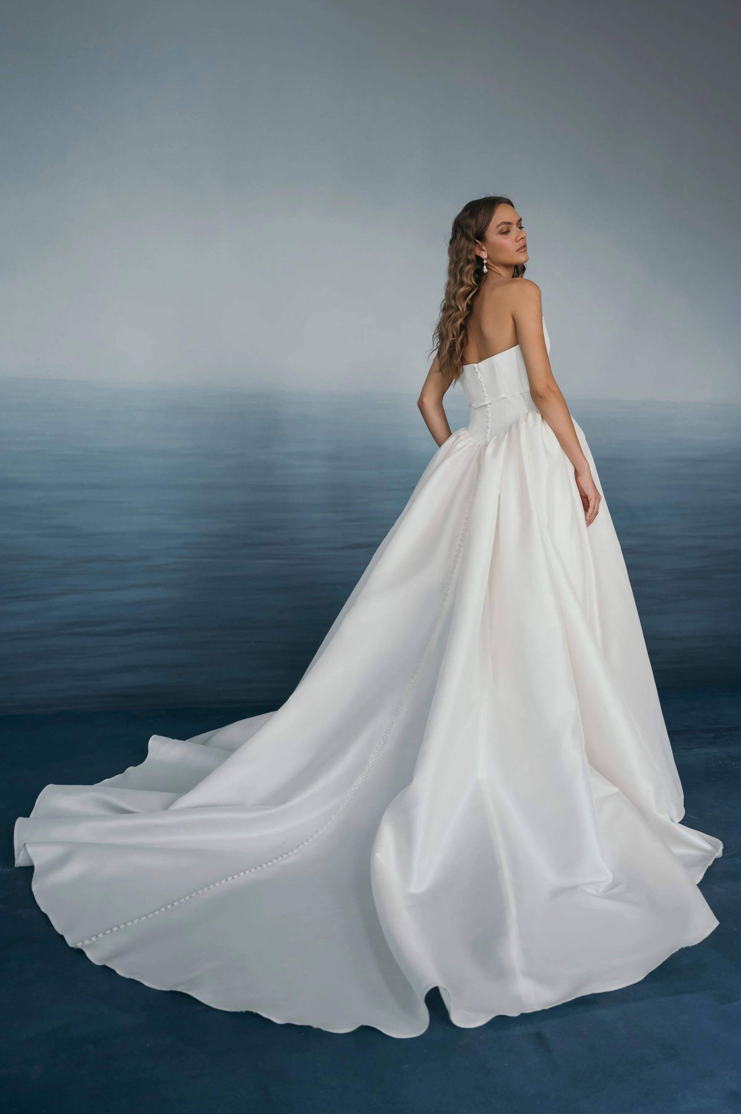 The Jenny Yoo Danielle gown is a romantic Italian taffeta ball gown with a fully corseted bodice and a striking high, peaked scoop neckline that creates a confident, flattering silhouette. It’s balanced by a voluminous gathered skirt, delicate bow sa