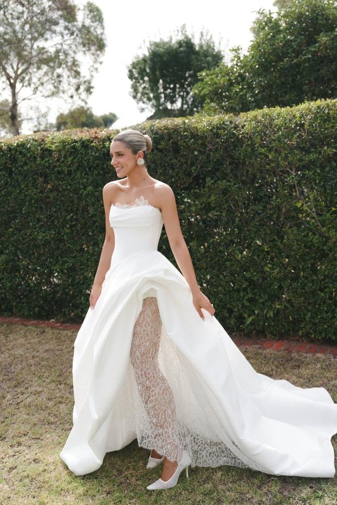 The Mariana Hardwick Maxine Wedding Dress is effortlessly modern with a timeless edge. Designed for the cool, confident bride, this gown delivers a clean, sculpted silhouette with refined detailing that feels understated yet elevated. Crafted from lu