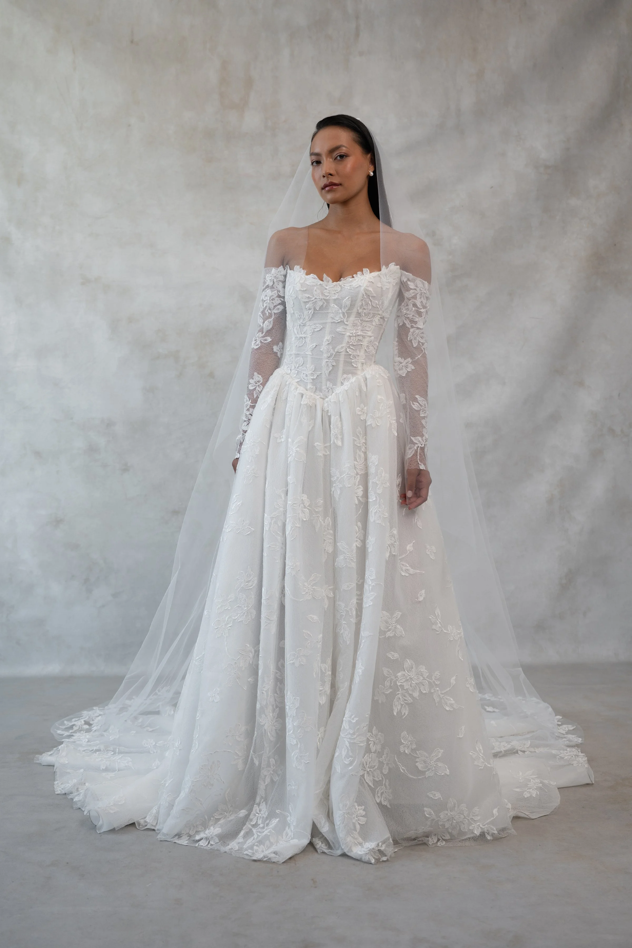 The Jenny Yoo Phoebe gown, cut in our delicately textured Isadora floral embroidery, is as modern as she is romantic. The structured Basque corset bodice leads way to a flowing gathered skirt. Detachable long sleeves lend exciting versatility.