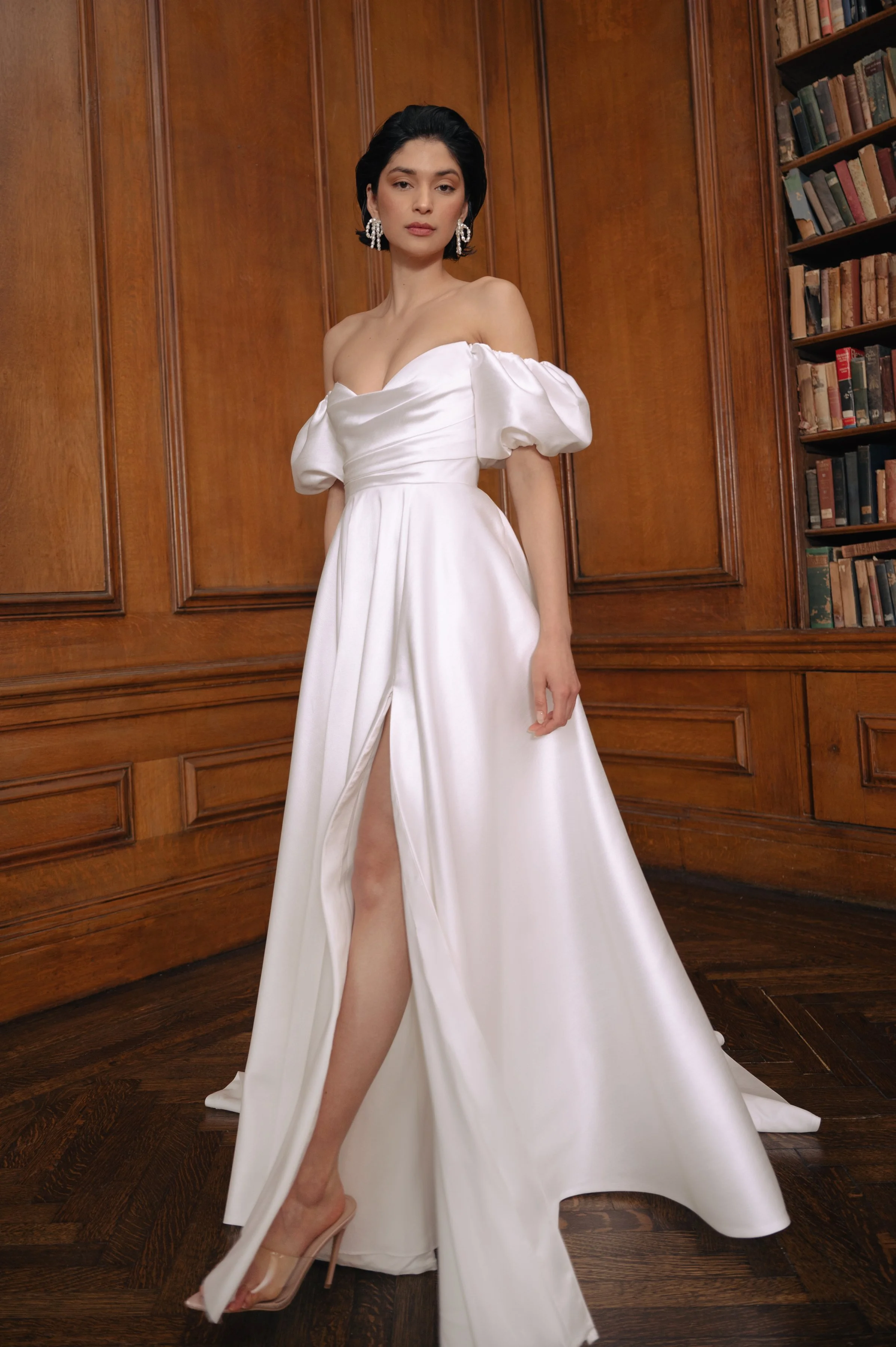 The Jenny Yoo Marisol gown is a romantic satin ball gown with a beautifully draped bodice and a sultry, sculpted cowl neckline that feels effortlessly feminine. It features a full skirt interrupted by a flattering slit and comes with detachable puff 