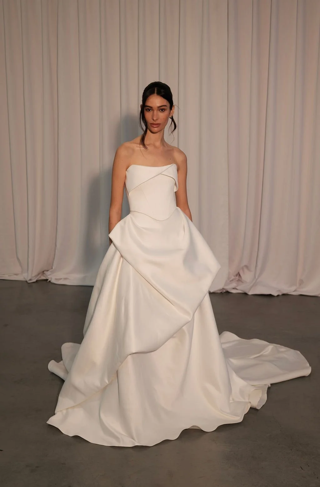 KYHA Bride Preston: an ode to eras past. A fresh take on tradition, Preston brings a modern edge thanks to its structural draping, showstopping train and architectural dropped waist. Crafted from luxe silk satin, Preston’s strapless silhouette, struc