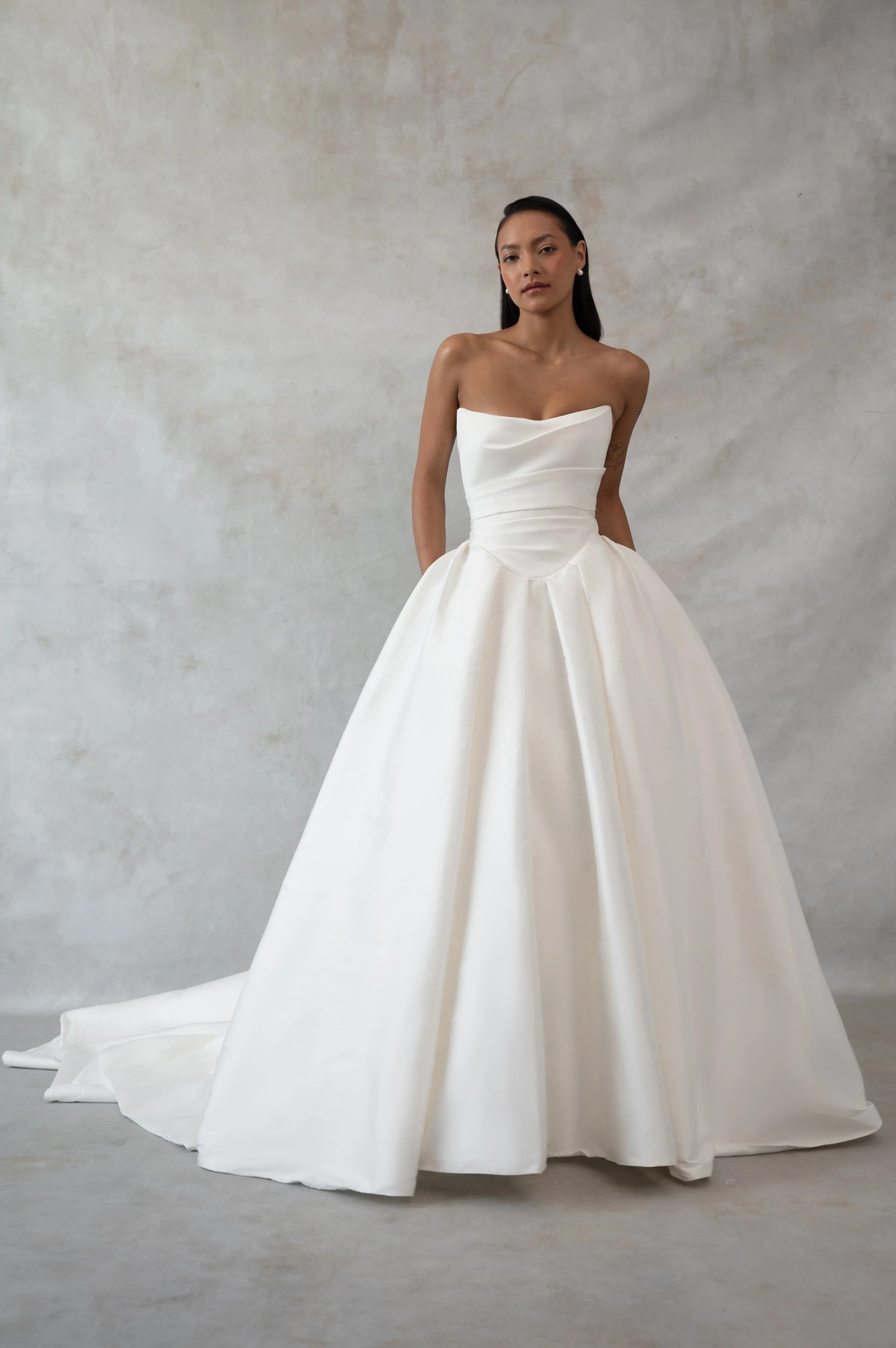 The Jenny Yoo Bridal Tristan gown is a study in striking simplicity. Cut in our favourite Italian taffeta. She features a delicately draped corset bodice, flattering Basque waist, and dramatic pleated ball skirt.