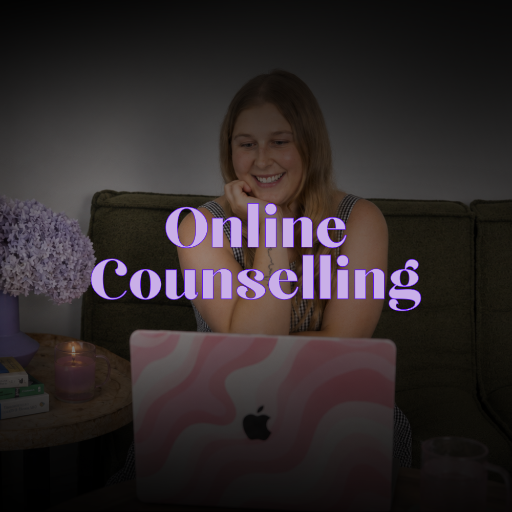 A woman smiling at her laptop screen during online therapy session, with purple flowers and a lit candle nearby, text overlay reads 'Online Counselling'.