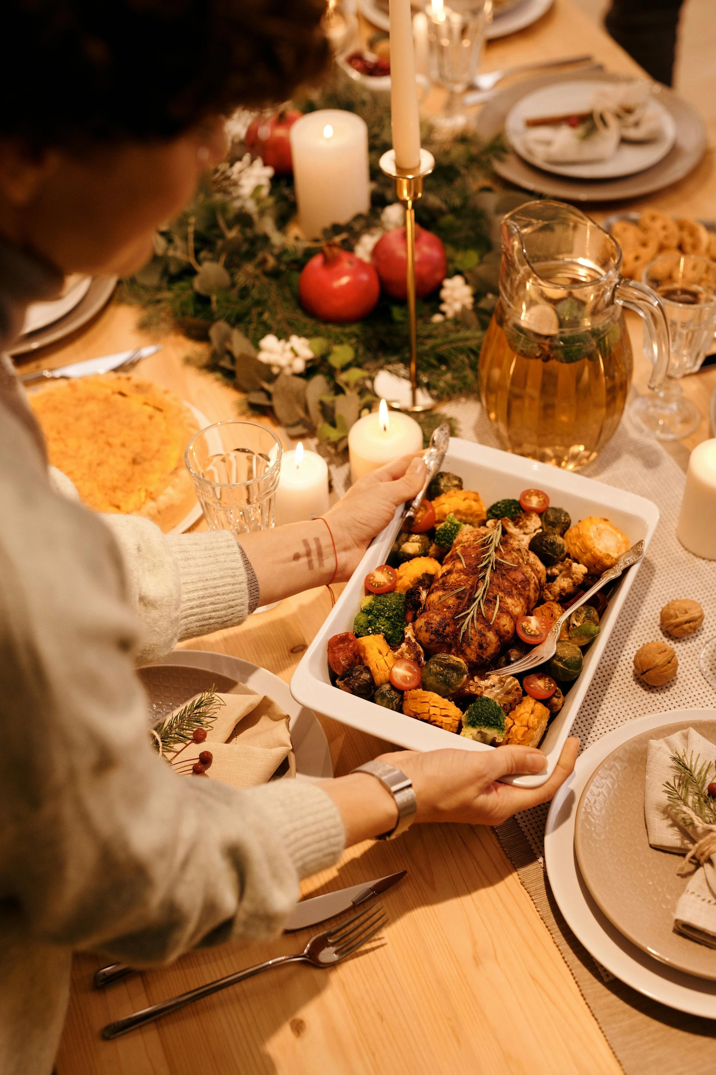 Festive dinner table with casserole dish of roasted chicken and vegetables, candles, and decorative wreath.