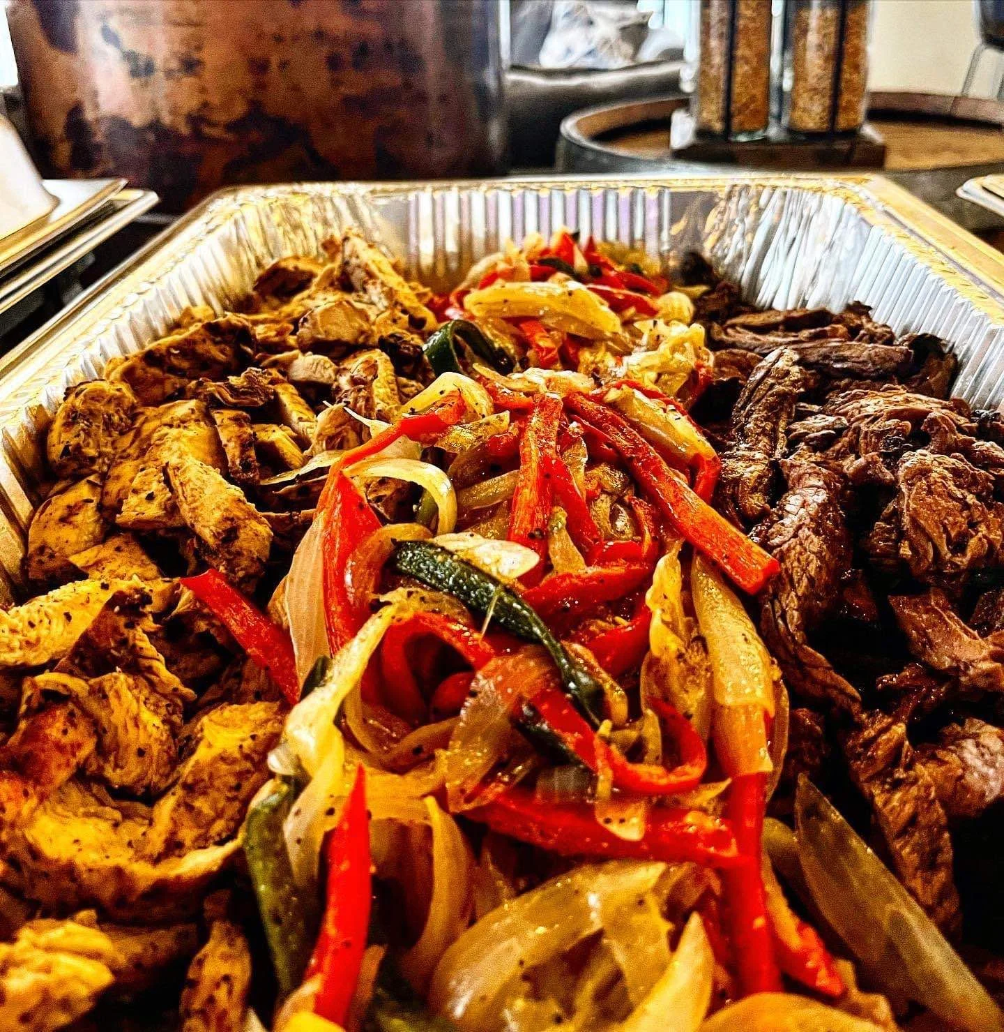 Tray of grilled fajita ingredients with chicken, beef, peppers, and onions.