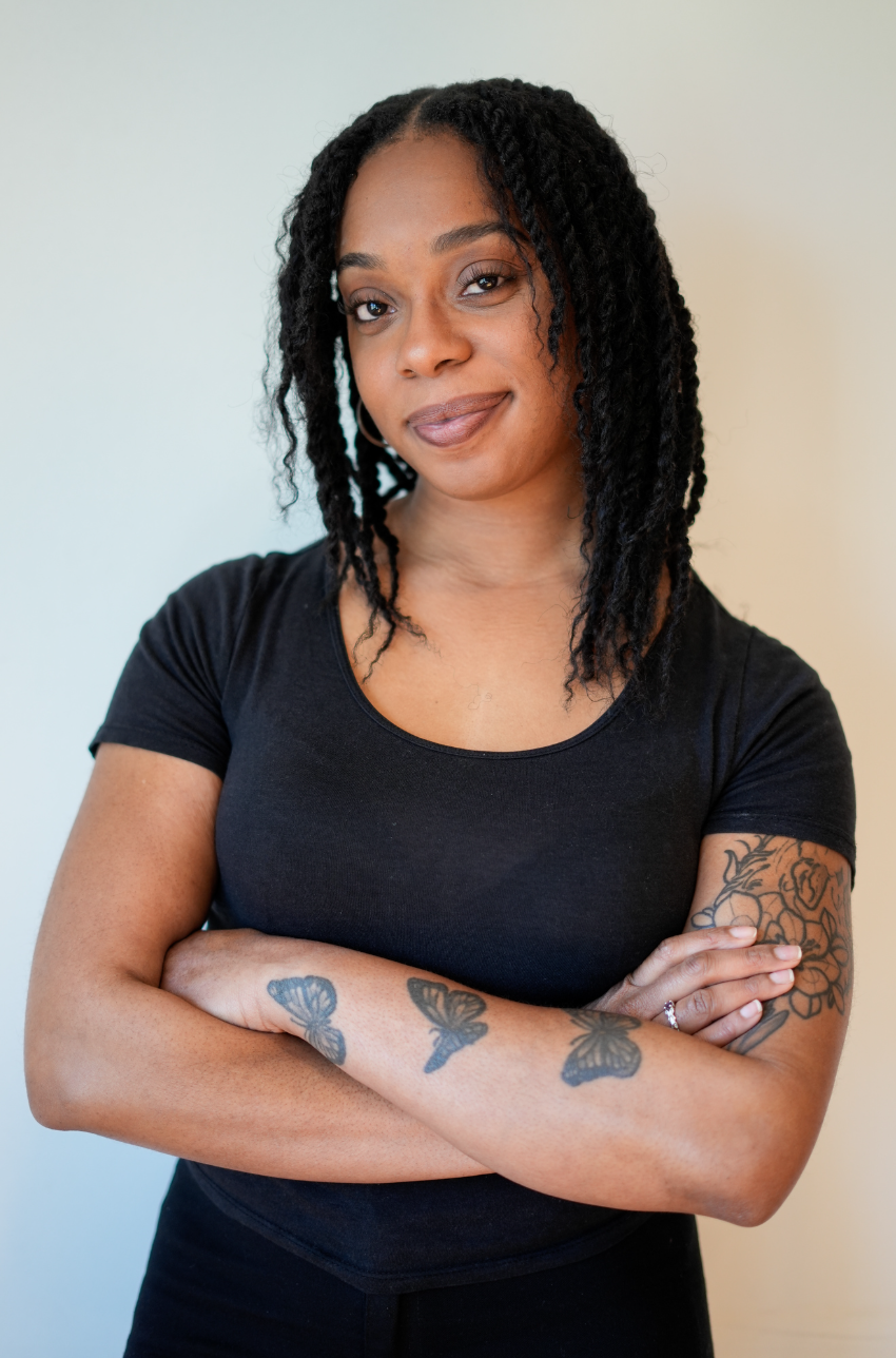 A woman with glasses and braided hair smiling at the camera, wearing a plaid coat.